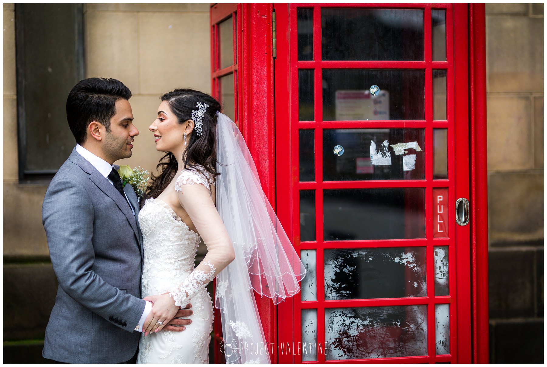 bride and groom cuddling by red phone box