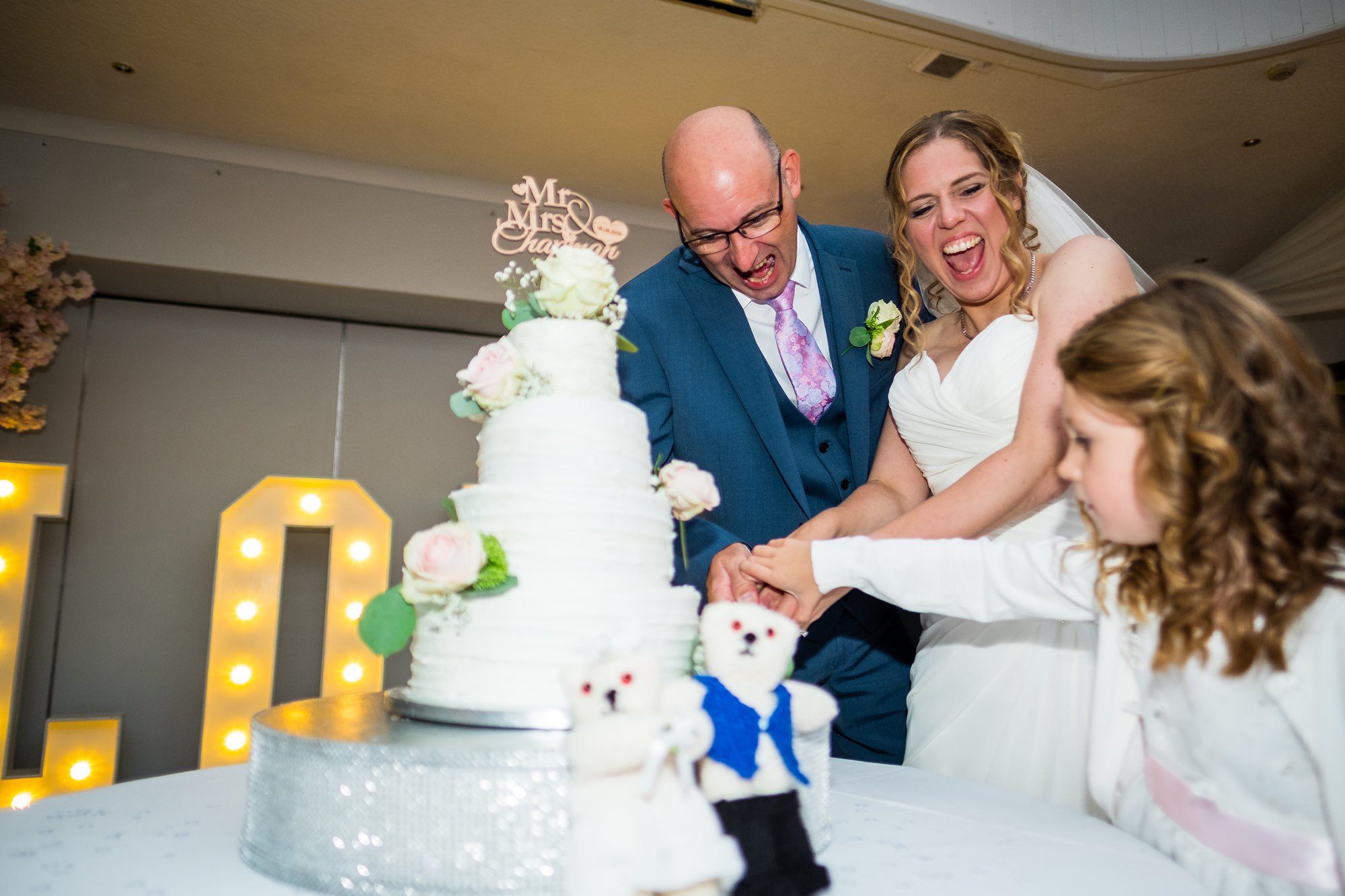 bride and groom cutting wedding cake with daughter