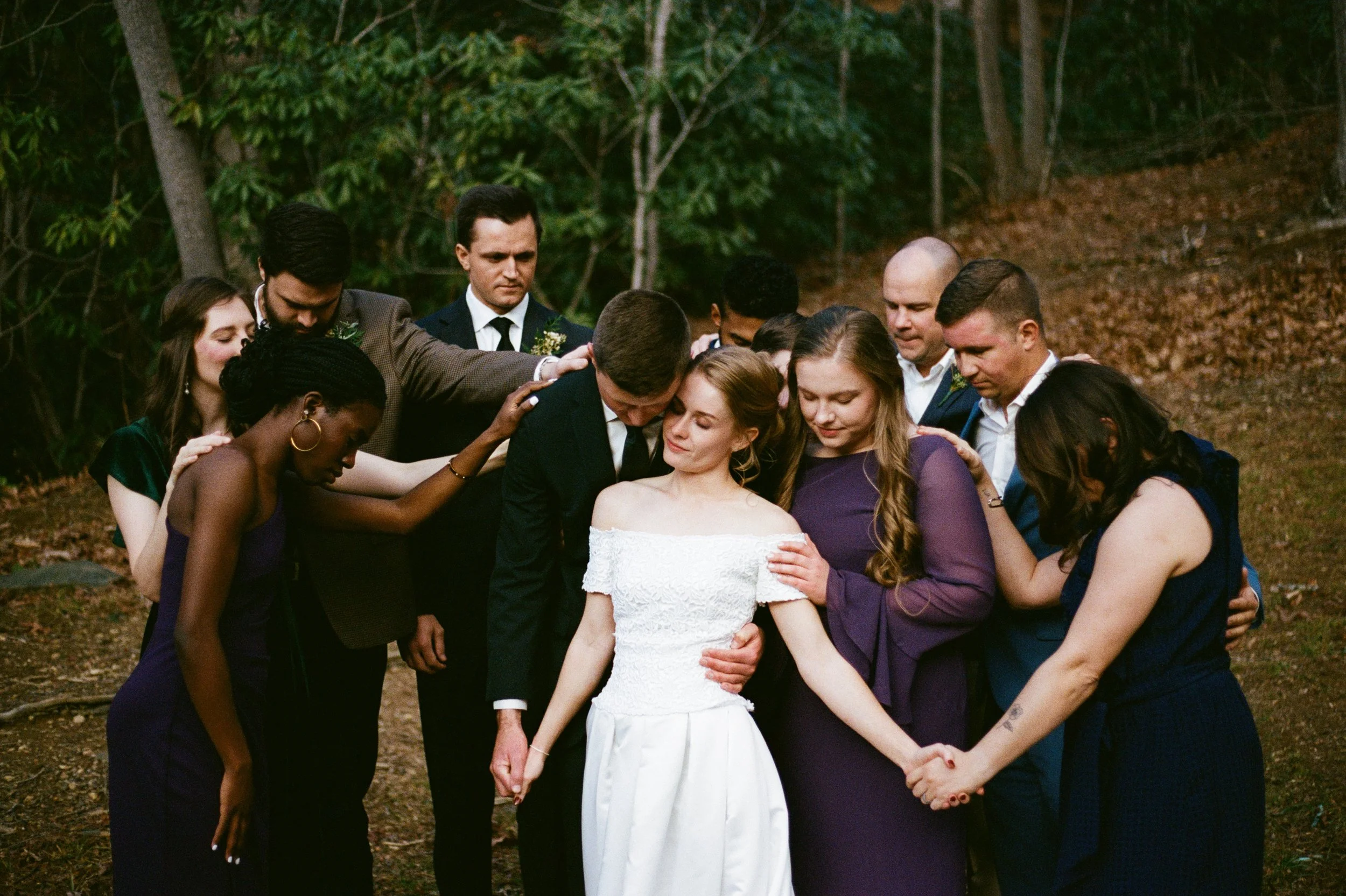 Film scan of a bridal party surrounding a bride and groom as they pray over them