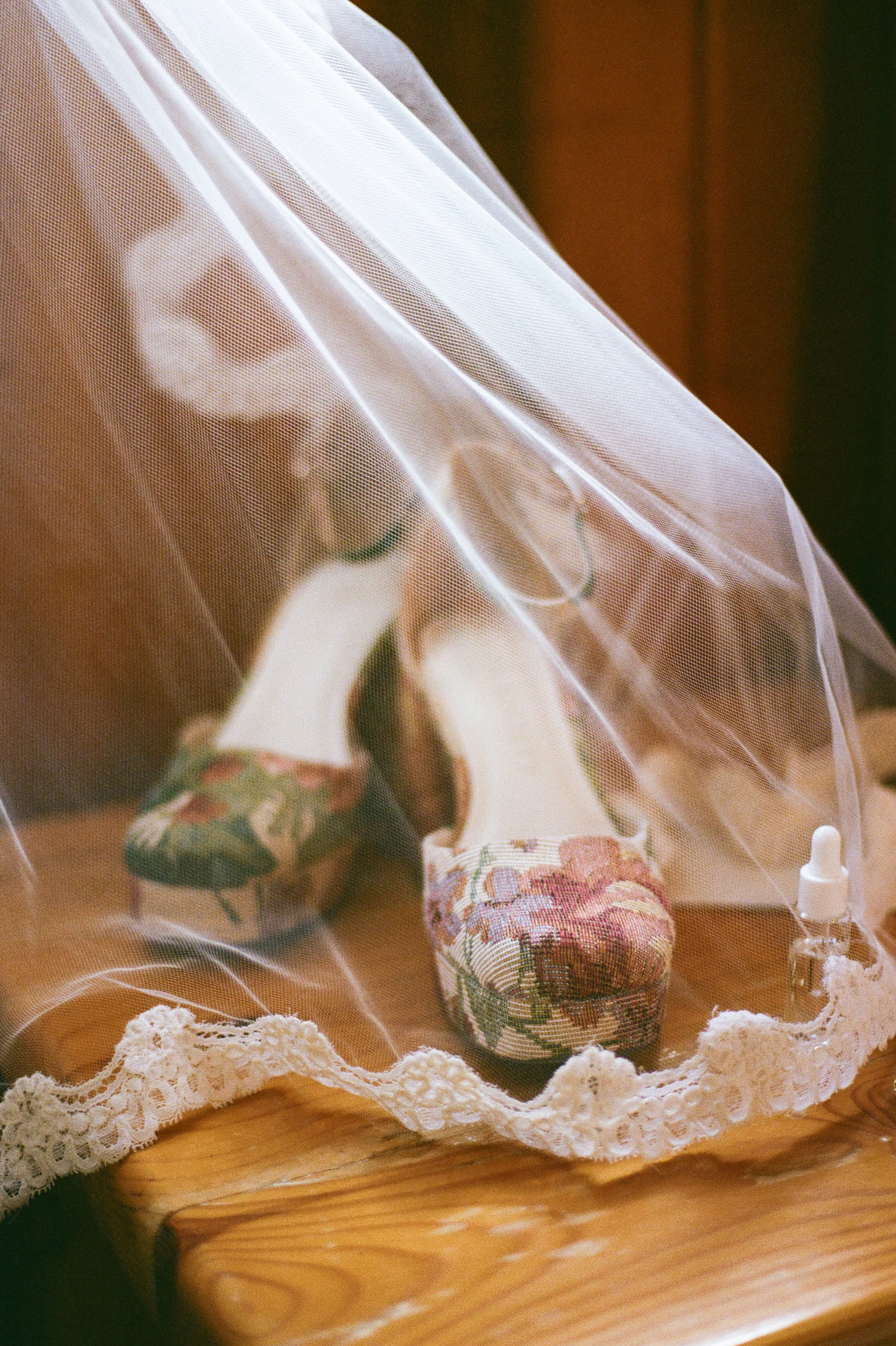 Bridal veil over top of wedding shoes and details on top of a wooden table.