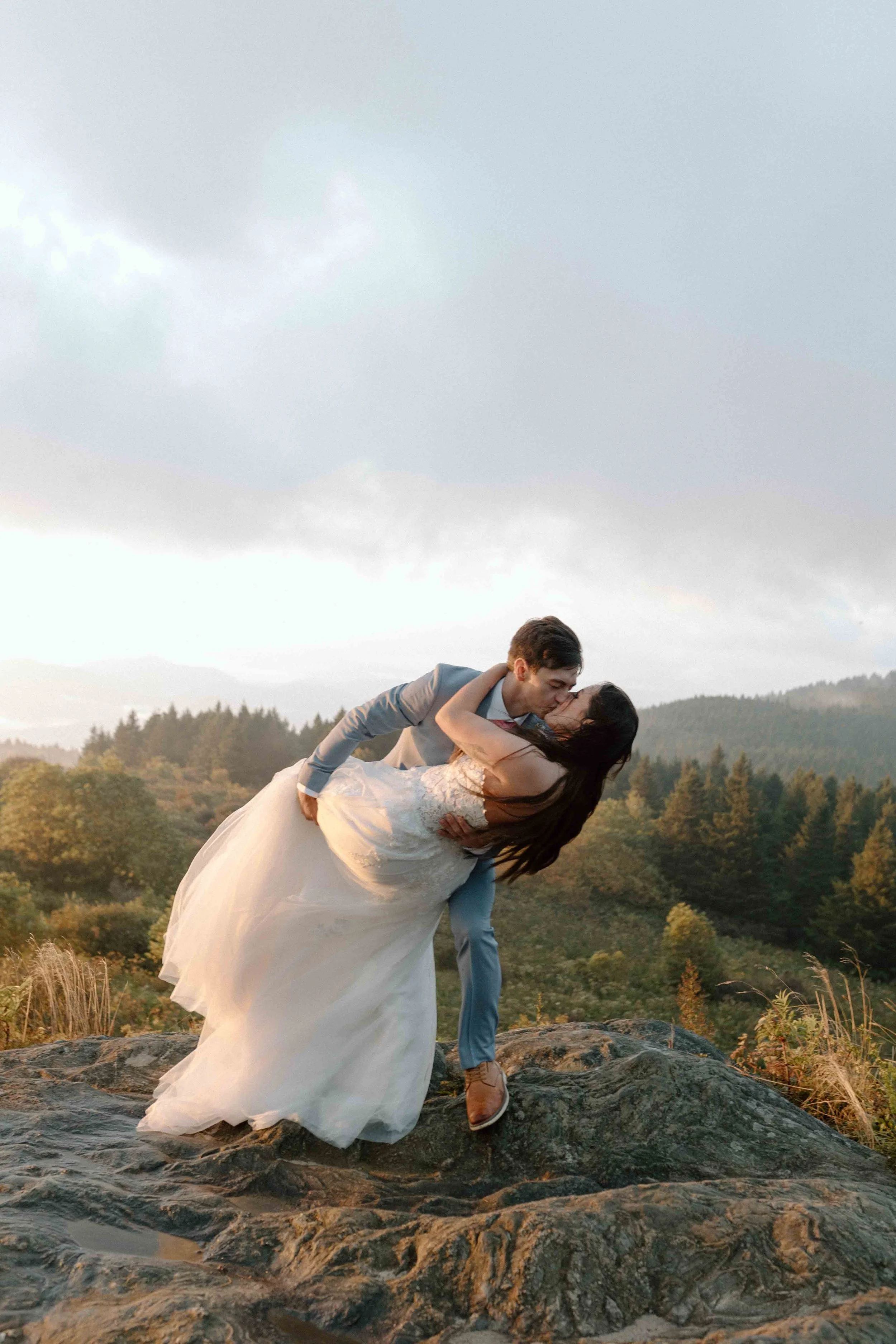 Overlooking a mountaintop, a groom dips his bride in a kiss.