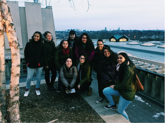 JCITs pose for a picture on the roof of Tisch Library where the city skyline is visible. (Left to right: Rachel, Destiny, Kathleen, Kiara, Taysha, Alejandra, Mara, Alex, Bella, Alicia).