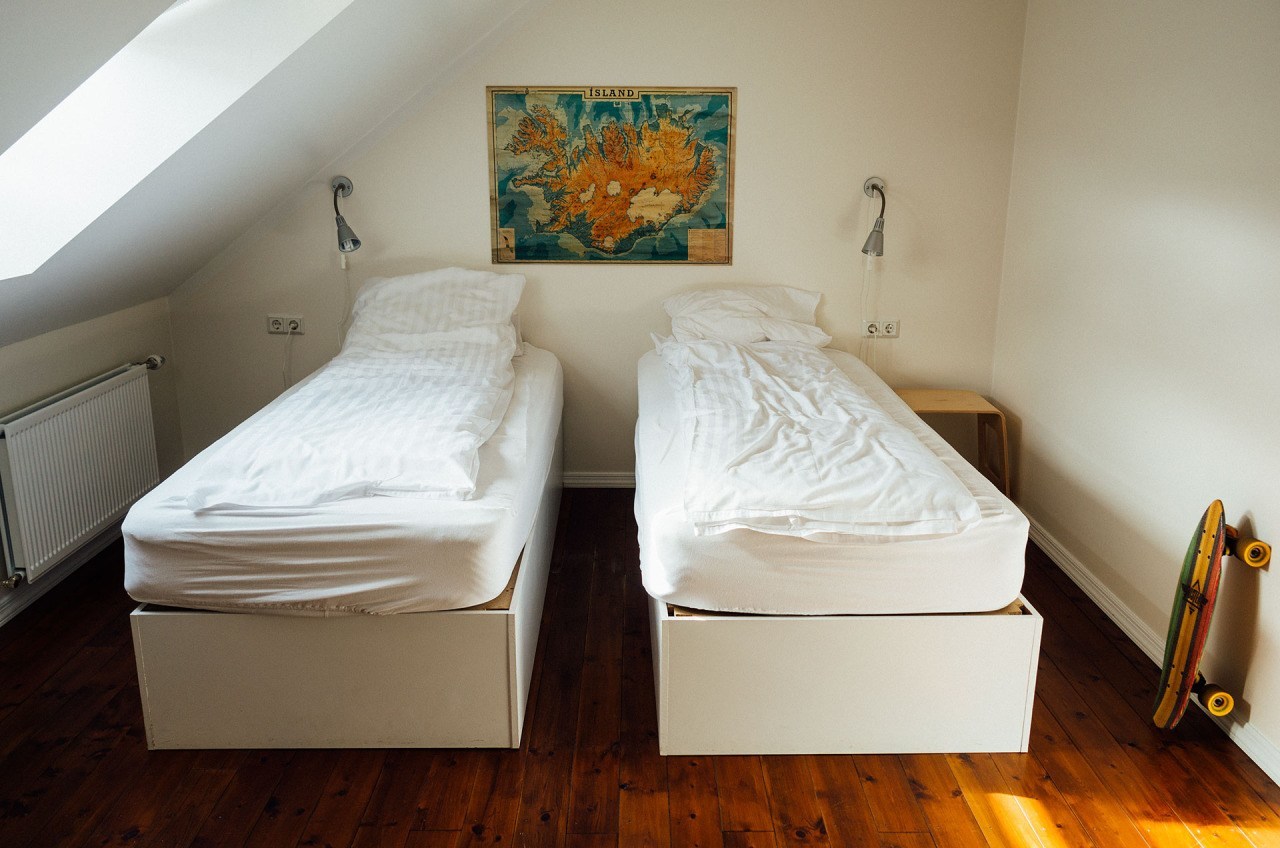 Two single beds in a room with messy sheets, a skateboard and a map on the wall