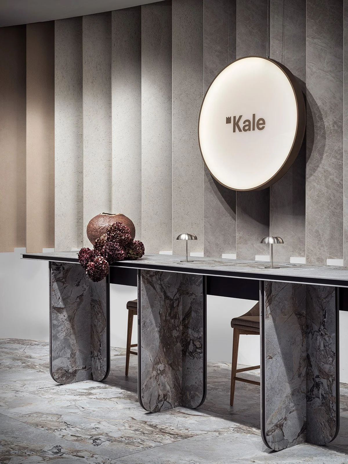  A reception desk of marble-effect ceramic slabs placed in front of a gradient wall of neutral-tone tiles. 