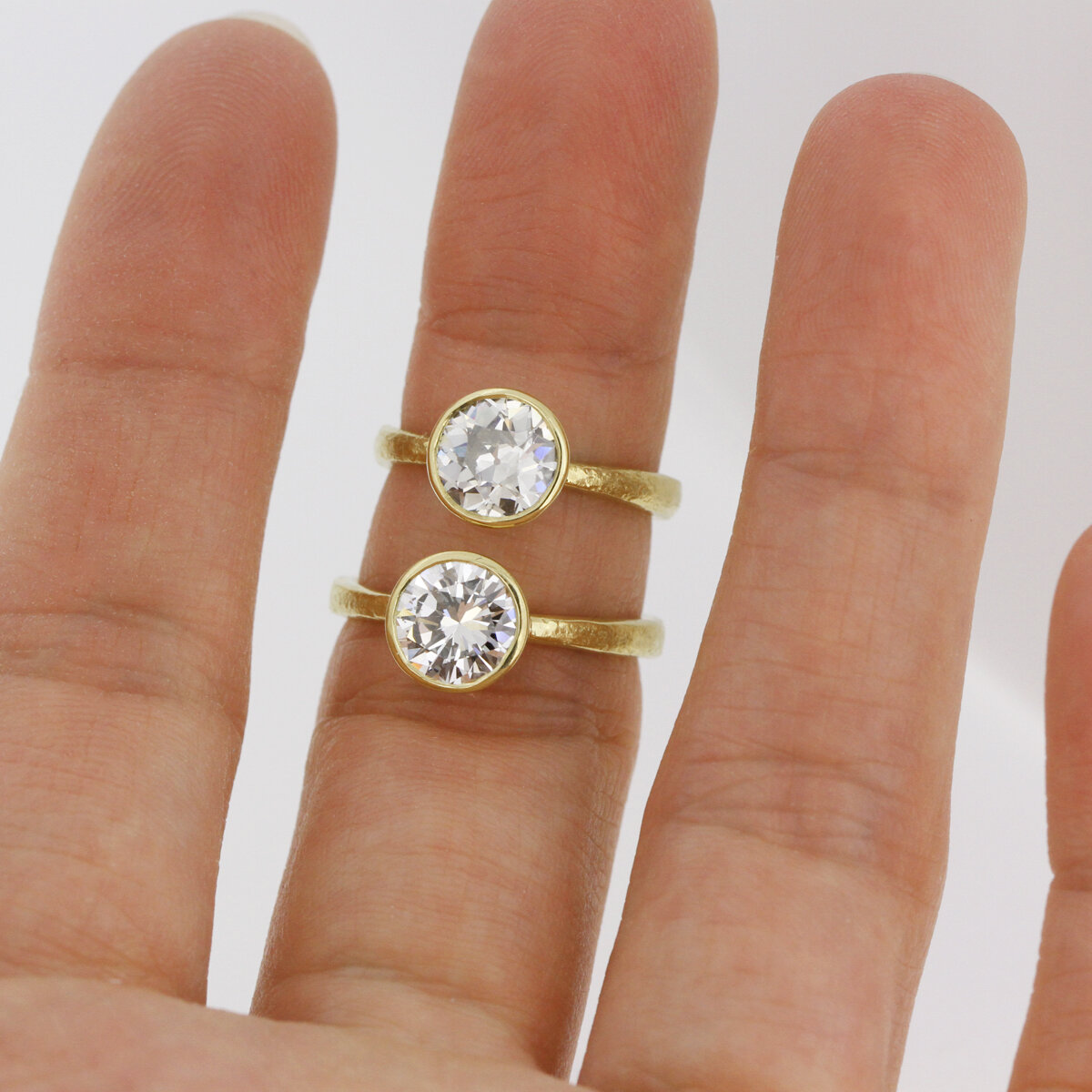 Old European on top, Round Brilliant on bottom. Notice the different facet structure. The top stone has chunkier facets and you can see the culet right at the center, while the bottom stone has slimmer facets. Both 18k Custom Rings by Sophie Hughes.