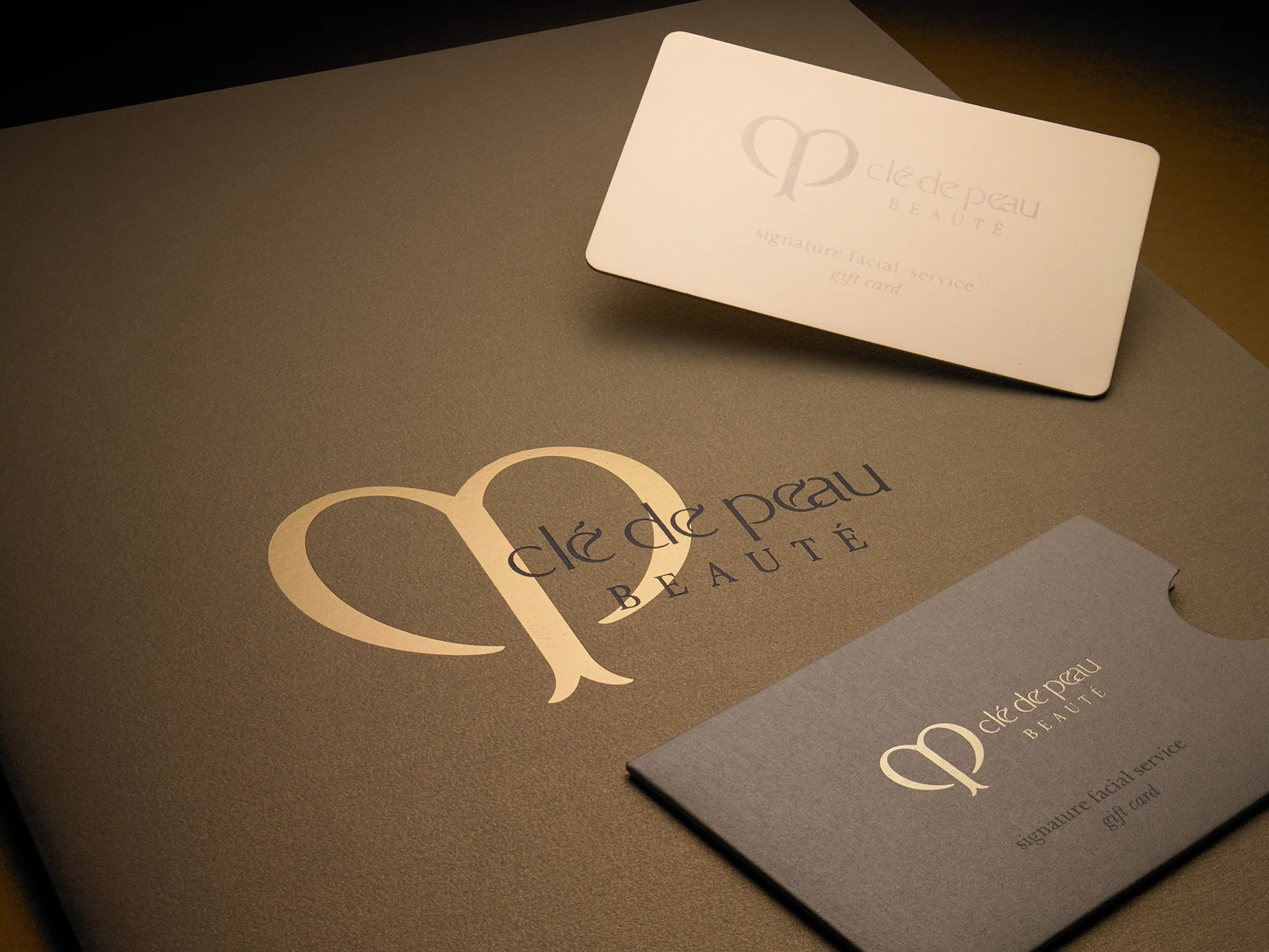 Clé de Peau Beauté Gift Card & Sleeve Clé de Peau is Shiseido’s high-end cosmetic brand. We made them a double-thick, foil-stamped gift card on gold foil cover stock to add a more substantial feeling to their promotion. The four corners were diecut round and the sleeve was printed on a pearlized cover sheet. Printing included a PMS gray and gold foil-stamped logo. It was diecut with a crescent thumb cut.