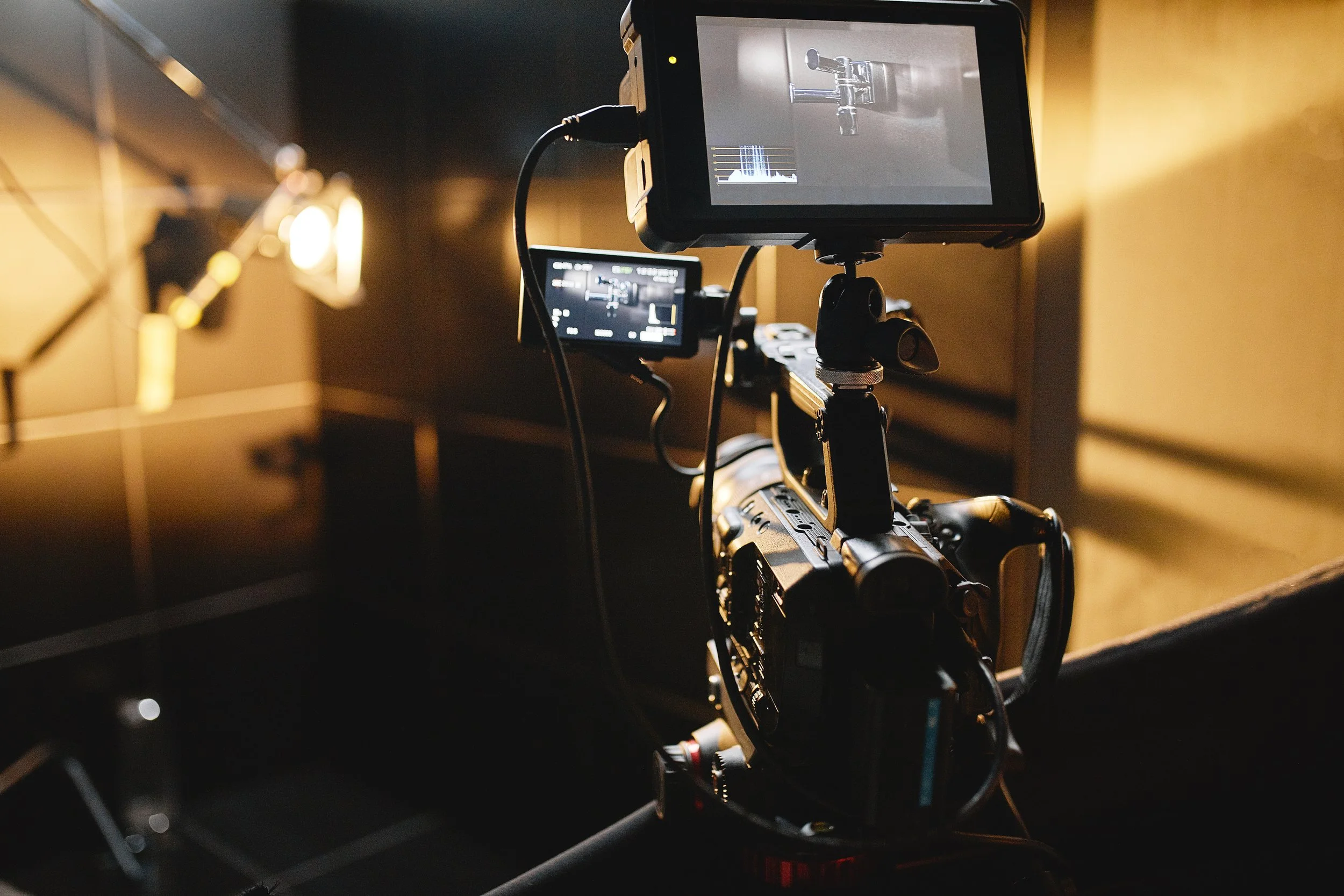 A professional camera setup with an external monitor and camera mounted on a tripod in a dimly lit room.
