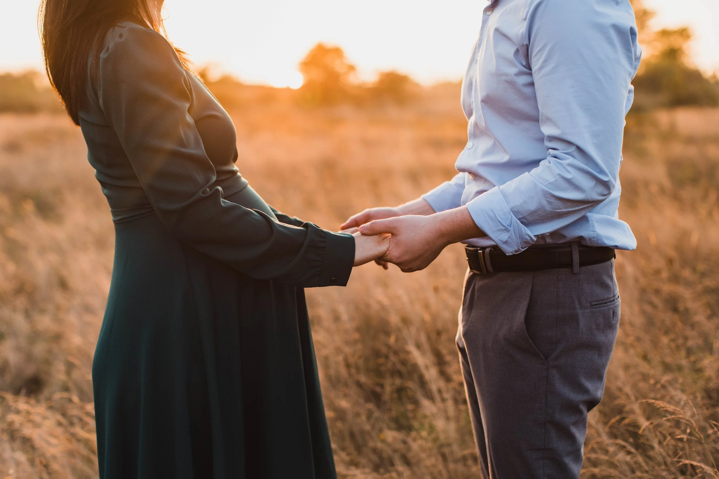A close-up of a couple holding hands over a pregnancy bump during a seattle maternity photography shoot at sunset.