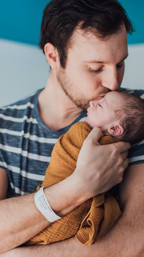   Seattle dad gently kissing his newborn’s head during a cozy, baby-led lifestyle session in a hospital room.  