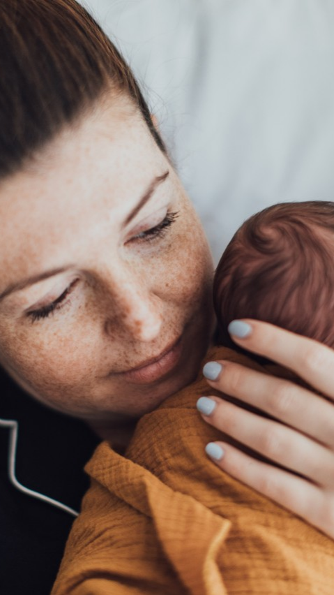  Seattle mom cradling her newborn baby close in soft morning light during an in-home newborn session. 