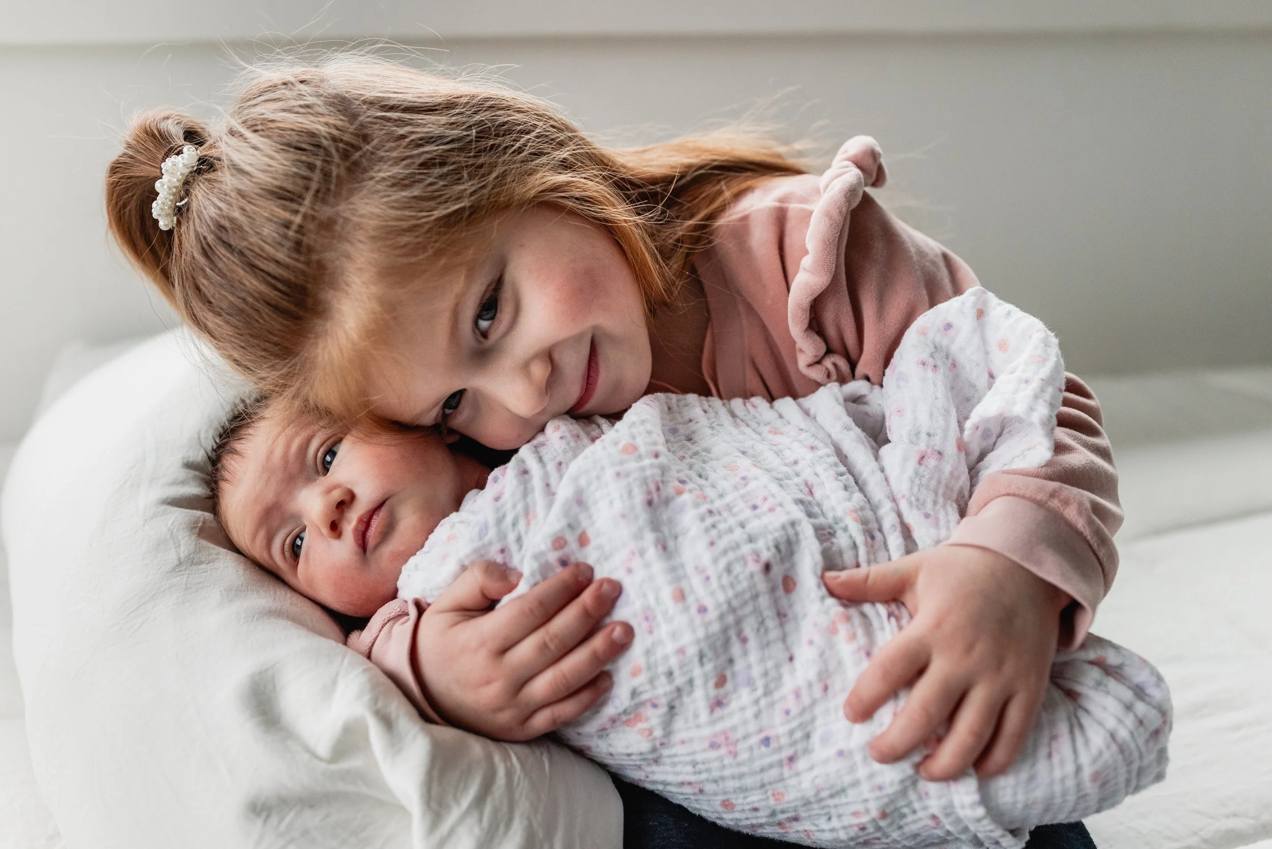 Big sister poses with Newborn sibling during an in home newborn photo session Seattle area