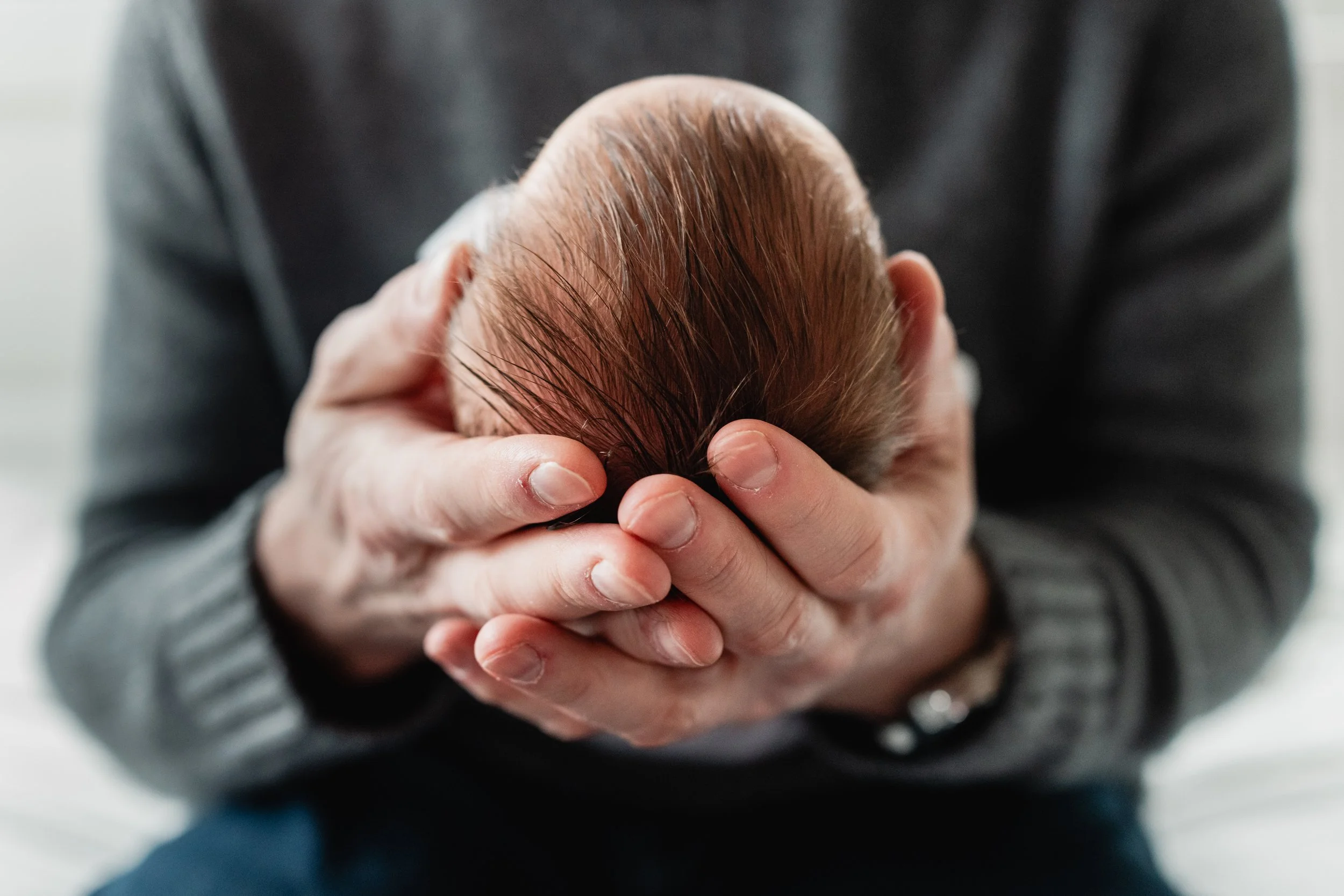 Detail shot of dad cradling newborn in his hands.