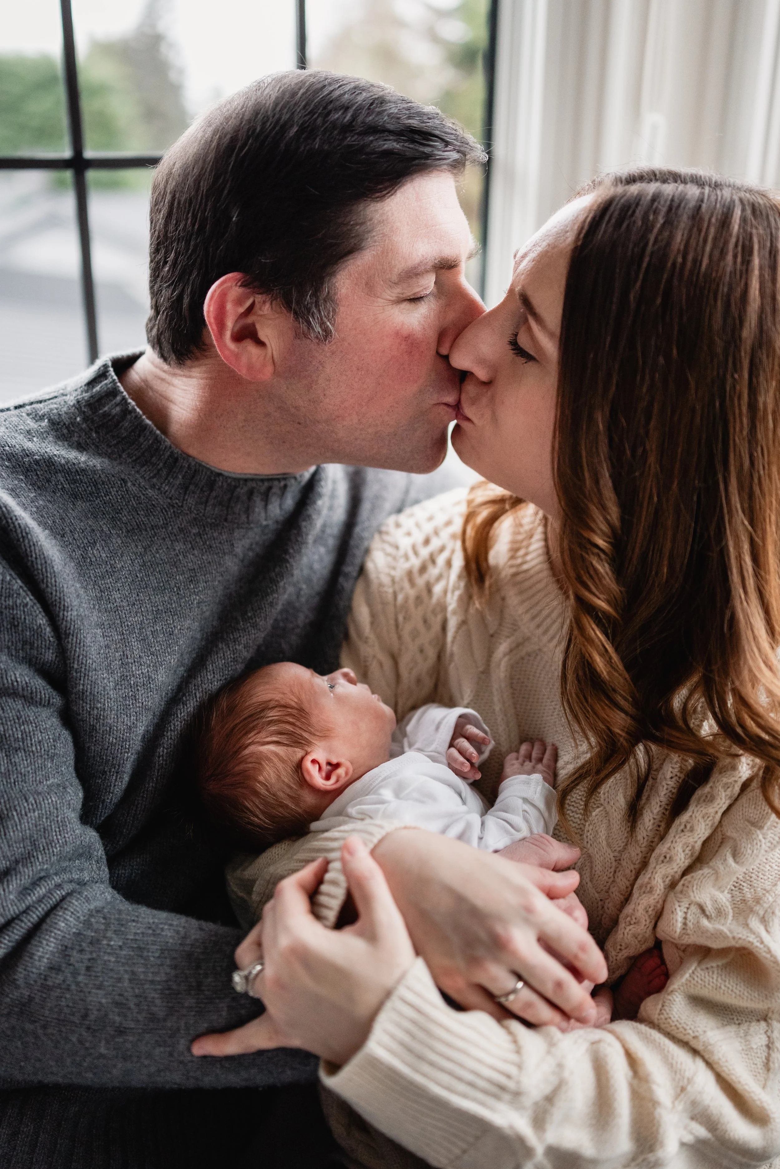 Mom and dad to newborn baby share a kiss during their lifestyle newborn session in seattle.
