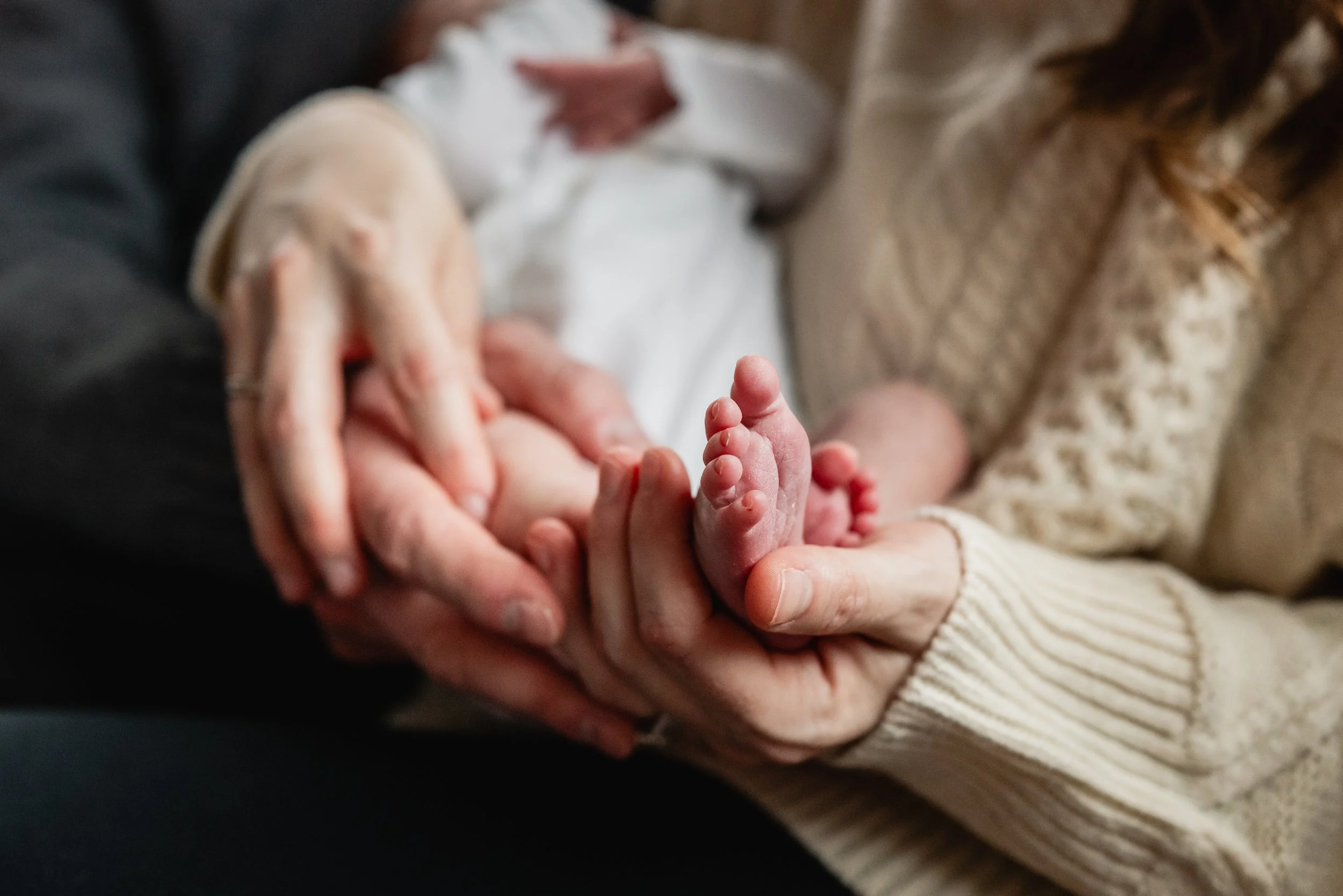 Close up details shot of parents holding newborn babies feet 