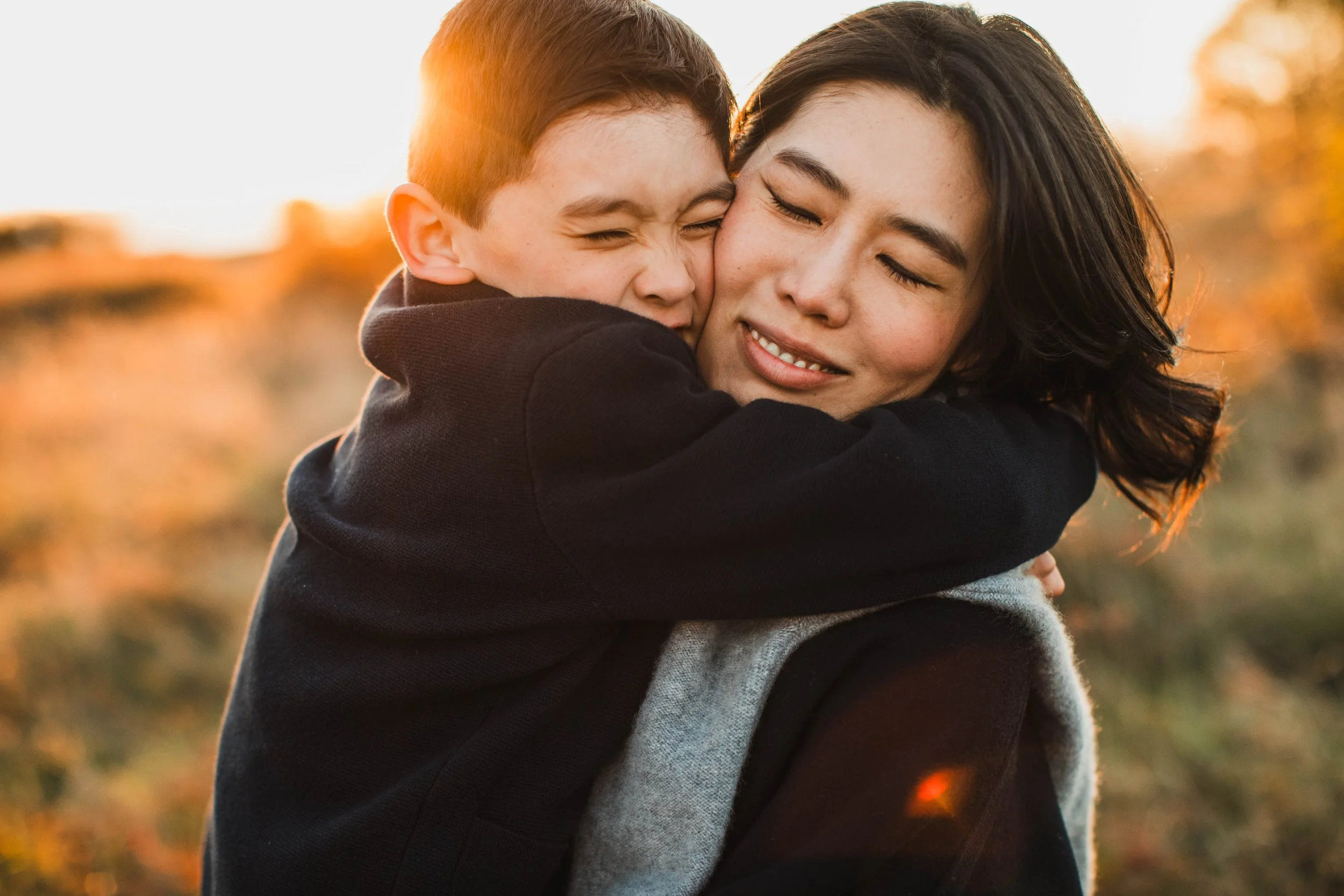 An intimate hug captured during a Seattle family photography session at Discovery Park with warm, sun-drenched lighting.