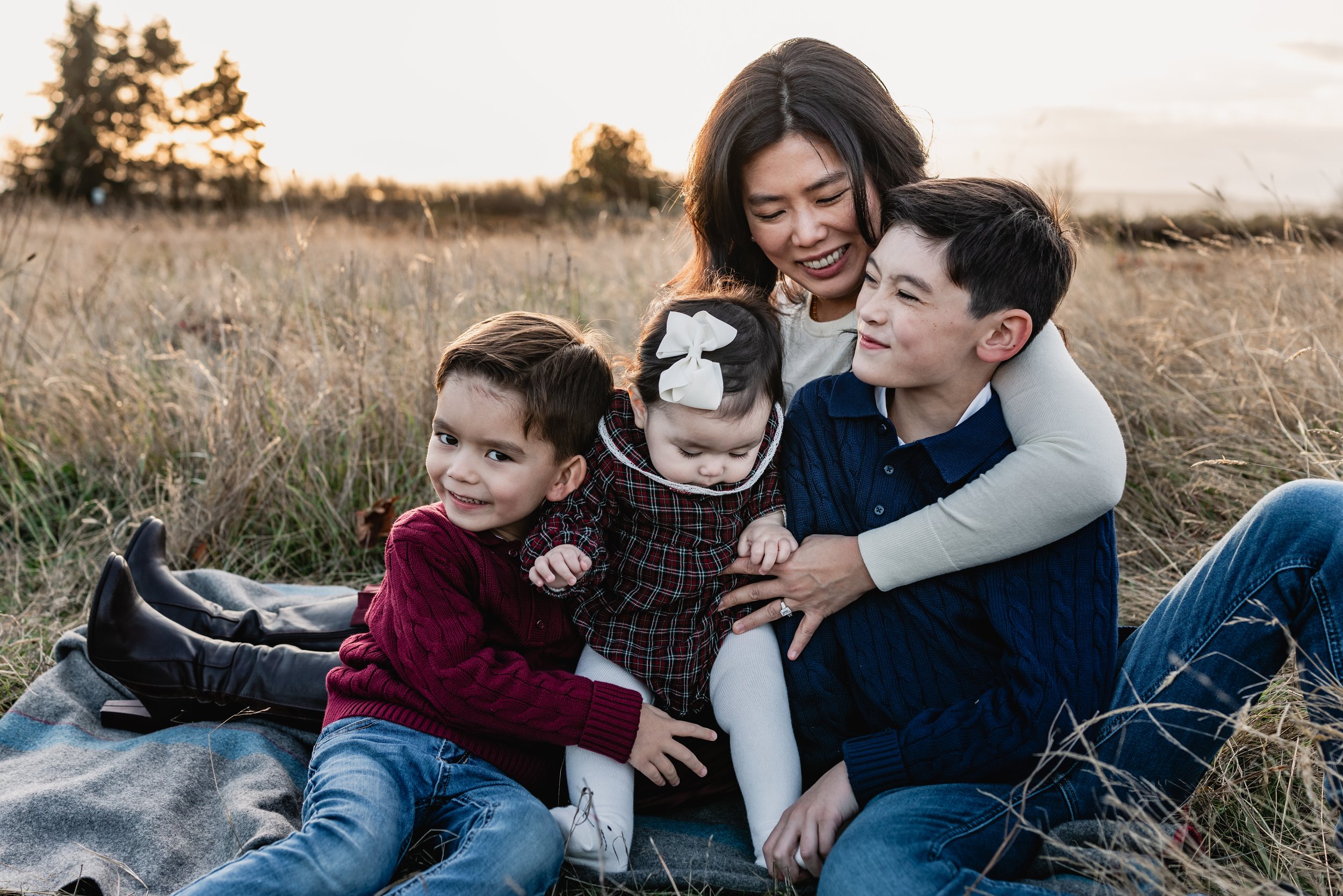 A mother sits on a blanket with her three children, gazing at her baby daughter in the center. A cozy moment from a fall Seattle family photography gallery.
