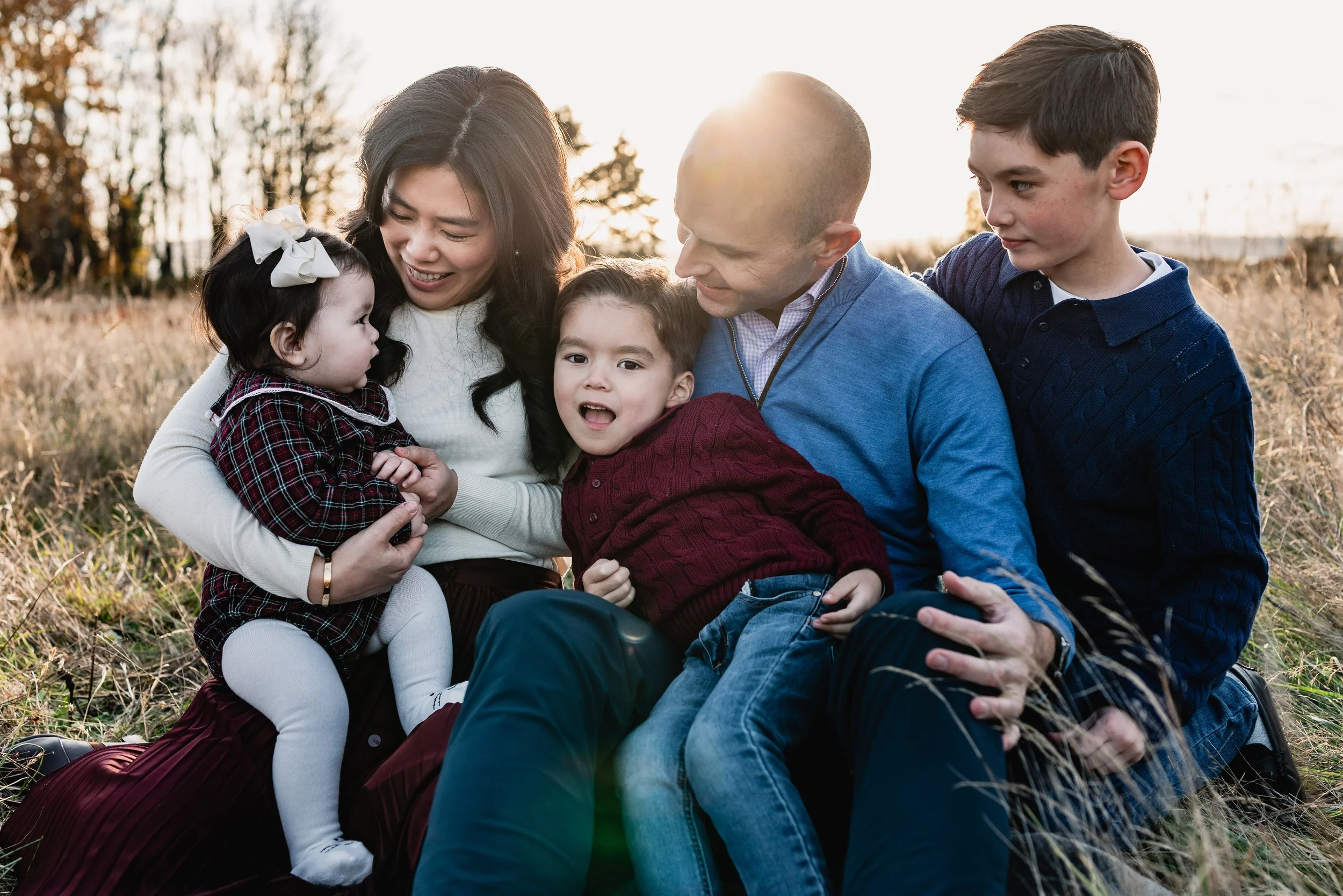 Close-up of a smiling family of five posing closely together on a blanket in a field. Professional Seattle family photography showcasing coordinated fall outfits.