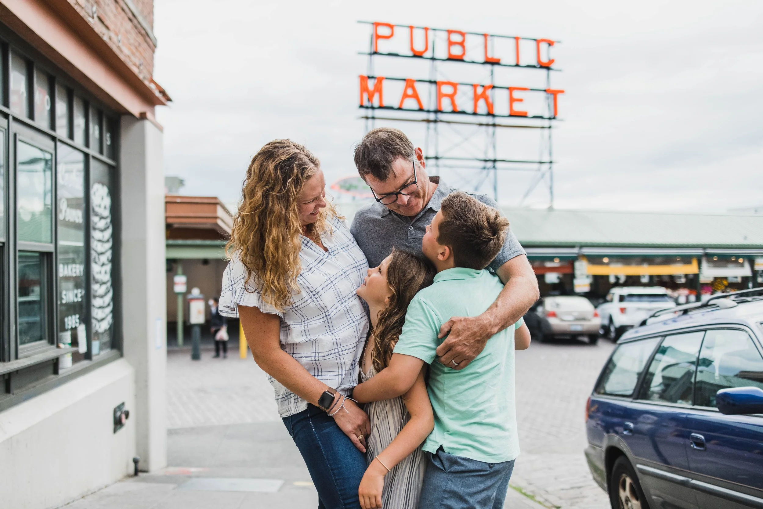 Seattle family photography, Pike Place Market sign, candid family hug, urban lifestyle photography, downtown Seattle.