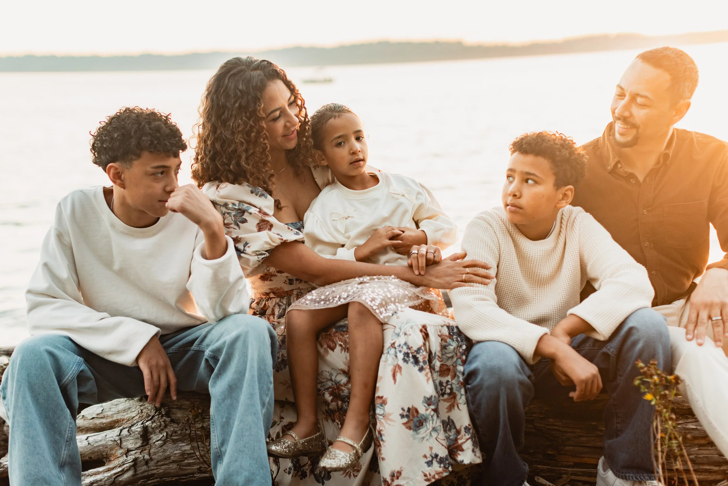 Seattle family sit on a drift wood log at the waters edge in West Seattle.