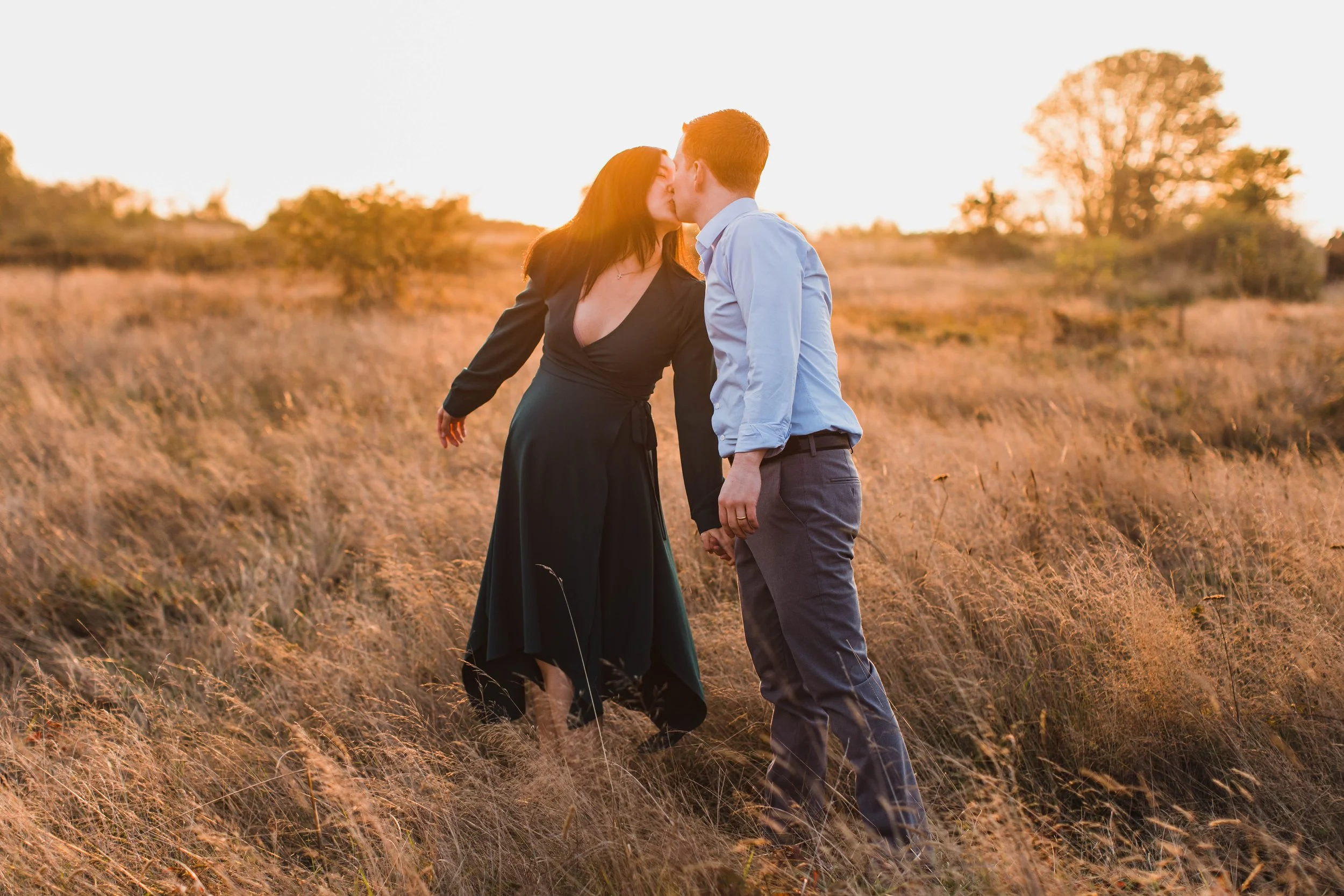 Expectant parents share a kiss in a sun-drenched field at sunset, captured by a professional seattle maternity photography specialist.