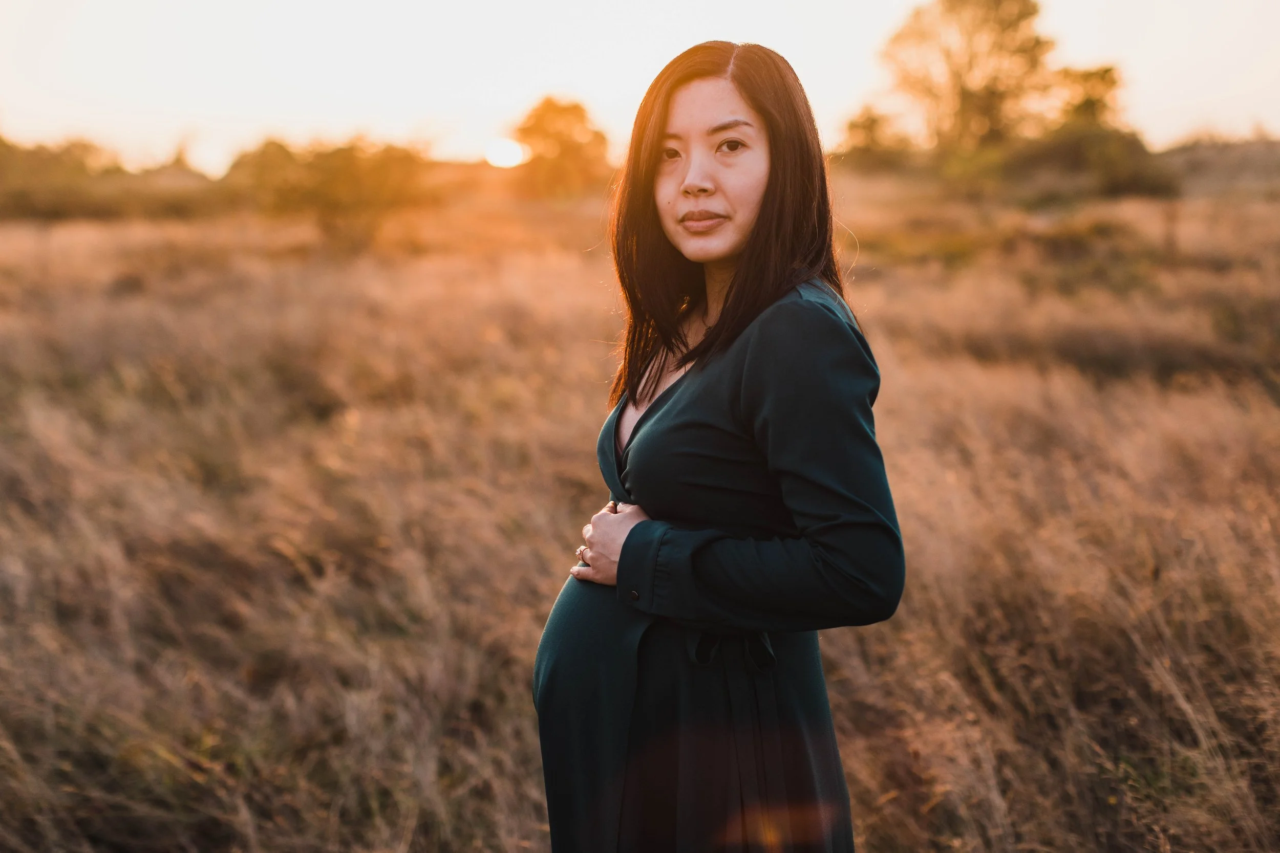 Portrait of a pregnant woman in a green wrap dress standing in a field for her seattle maternity photography session during the sunset golden hour.