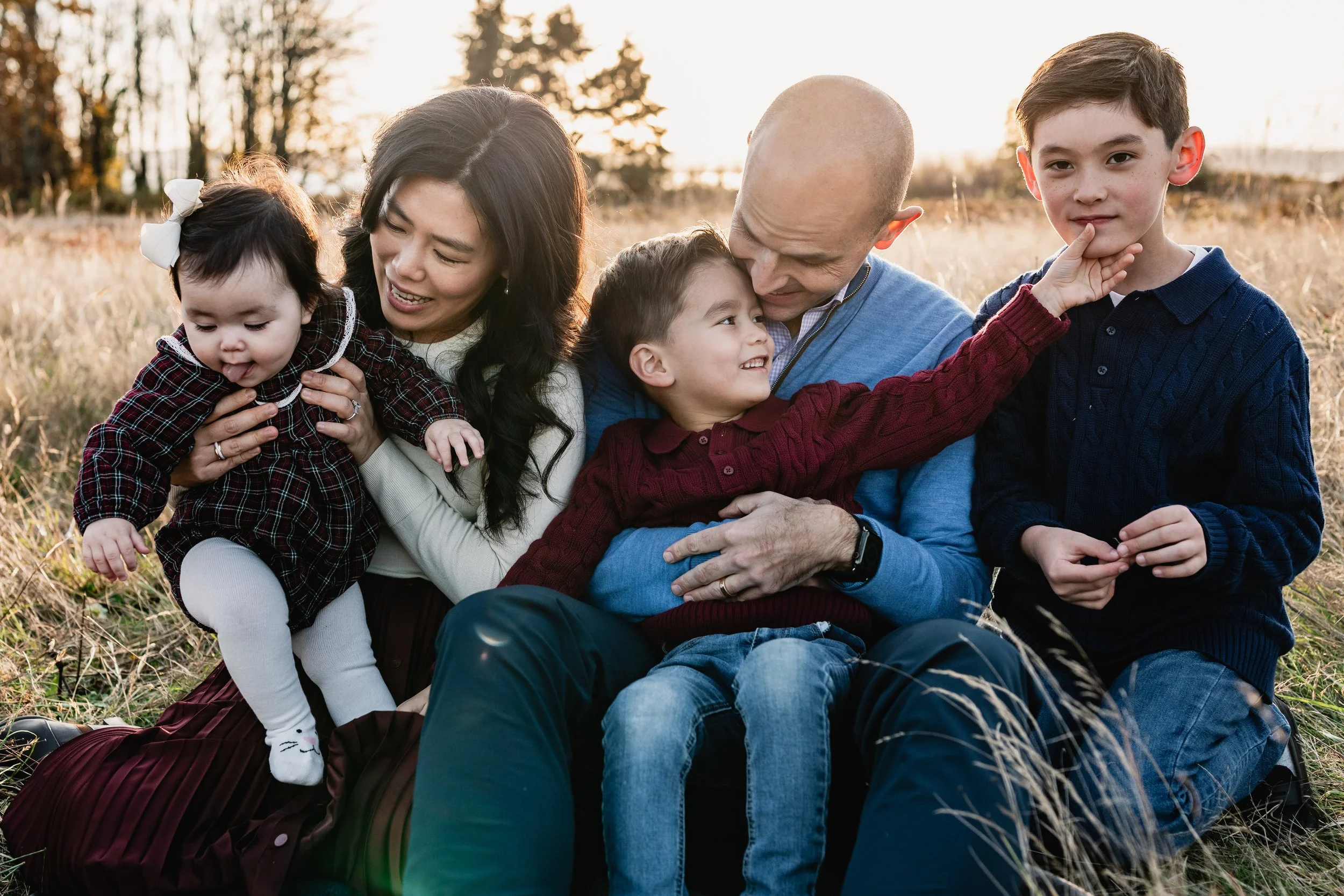 Expectant parents and their three children sit in the tall grass for a full-family portrait during a fall Seattle family photography shoot.