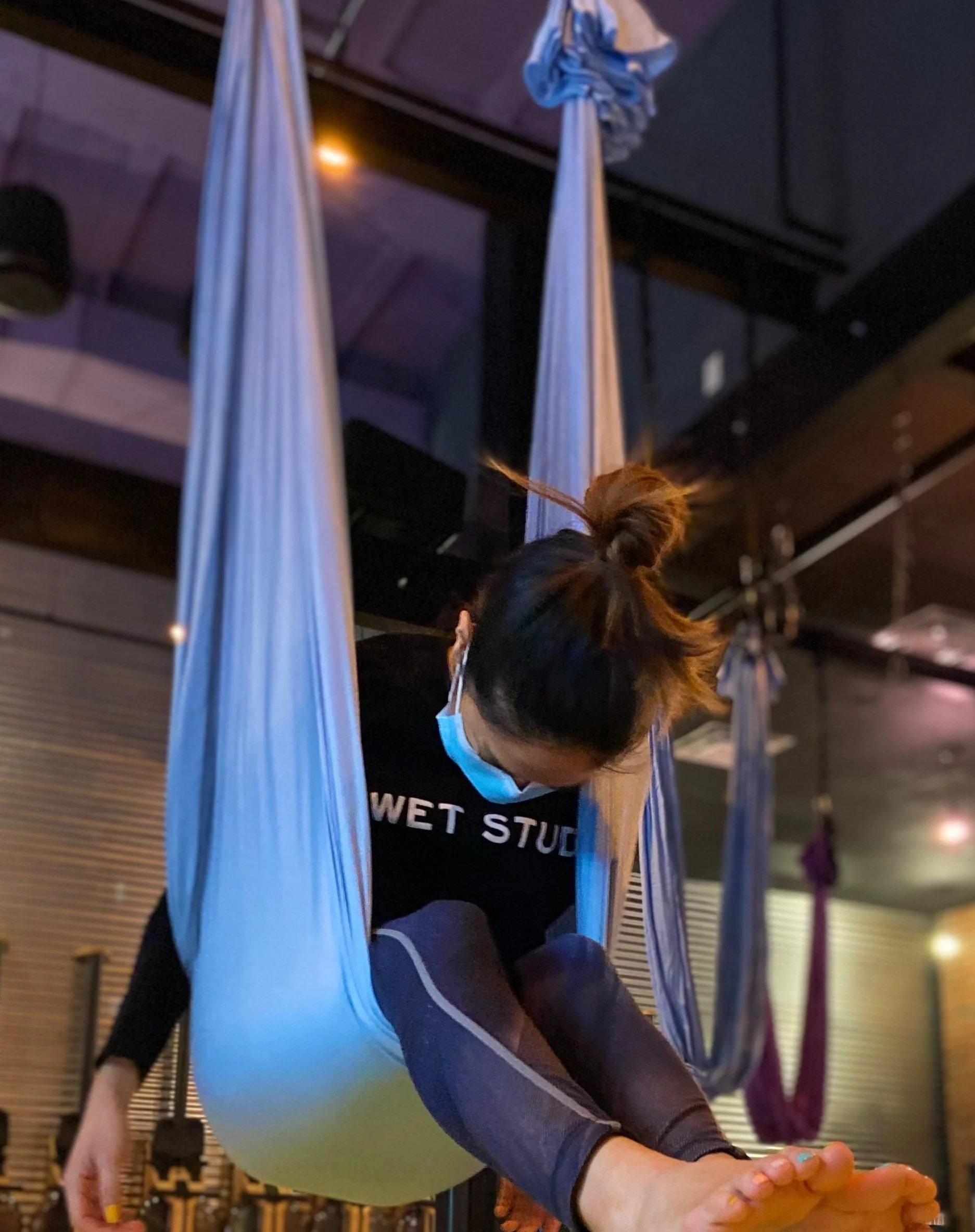 A woman suspended in the aerial hammock in a forward fold