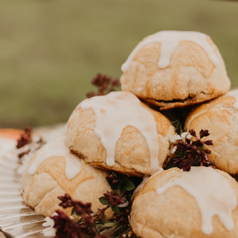Close-up of pastries topped with white glaze, garnished with small red flowers on a decorative plate.
