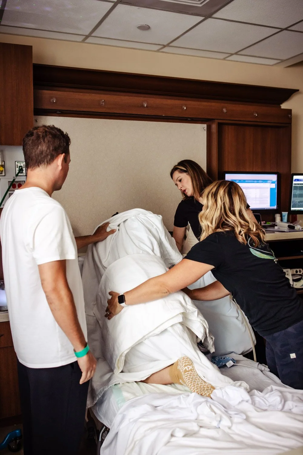 midwife and doula and husband support laboring woman at boca regional hospital while she kneels on all fours in the hospital bed