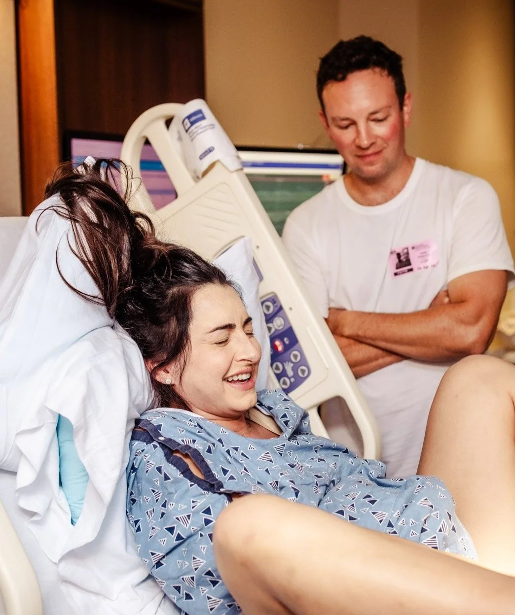 laboring woman smiles just before pushing baby out during vbac at boca raton hospital with husband in the background