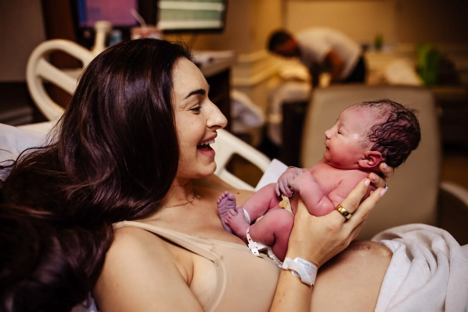 happy mother smiles and holds and greets her newborn baby girl in hospital  bed at boca regional labor delivery
