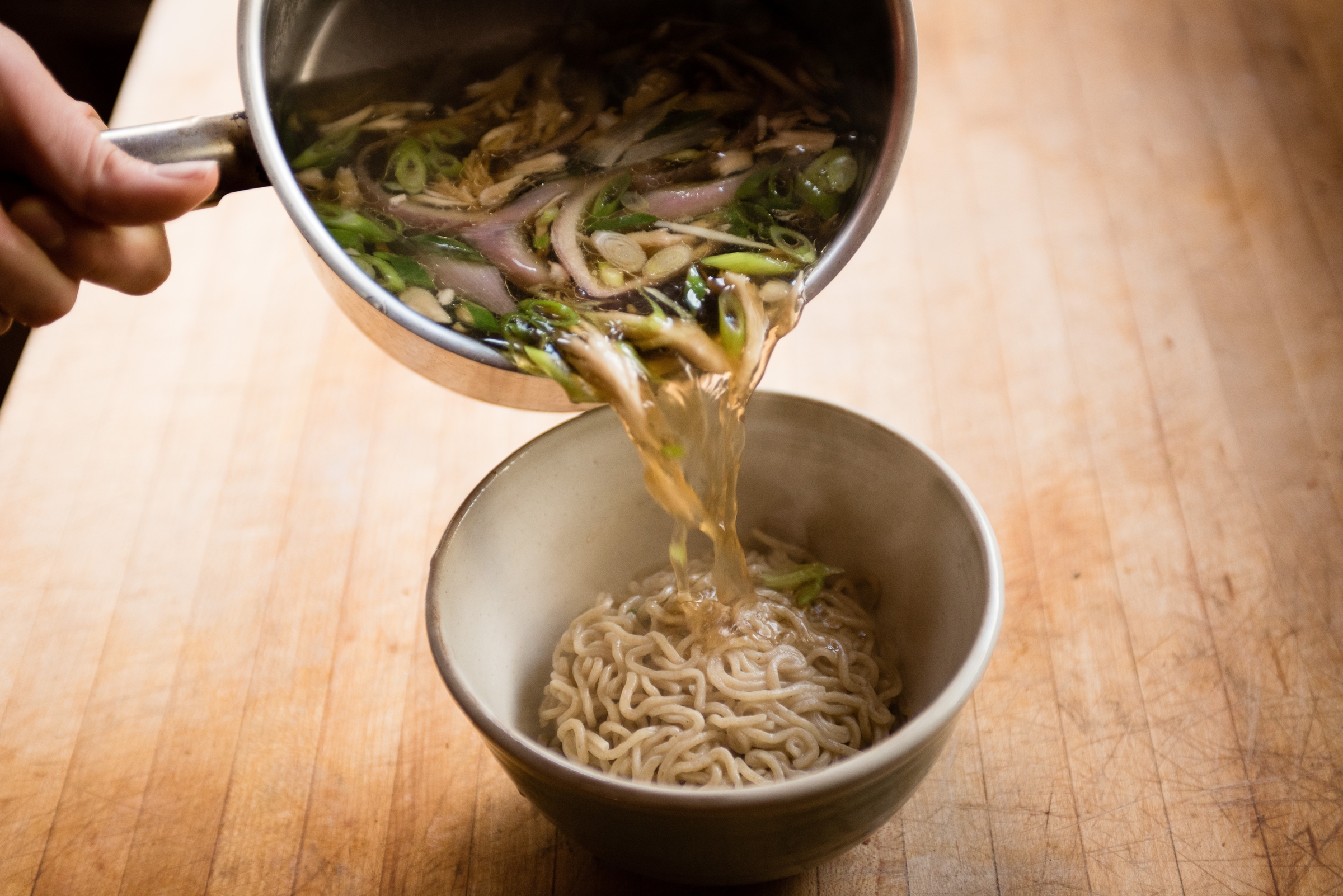 Pouring homemade chicken broth over Umi Organic fresh organic ramen noodles