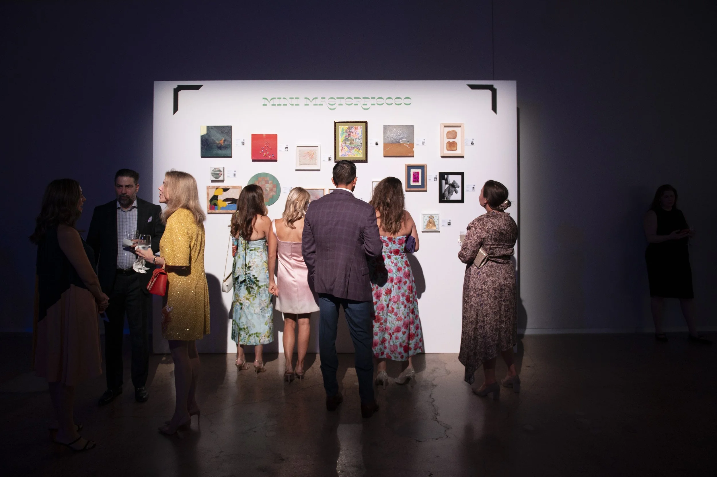 Attendees view a gallery wall with small artworks 
