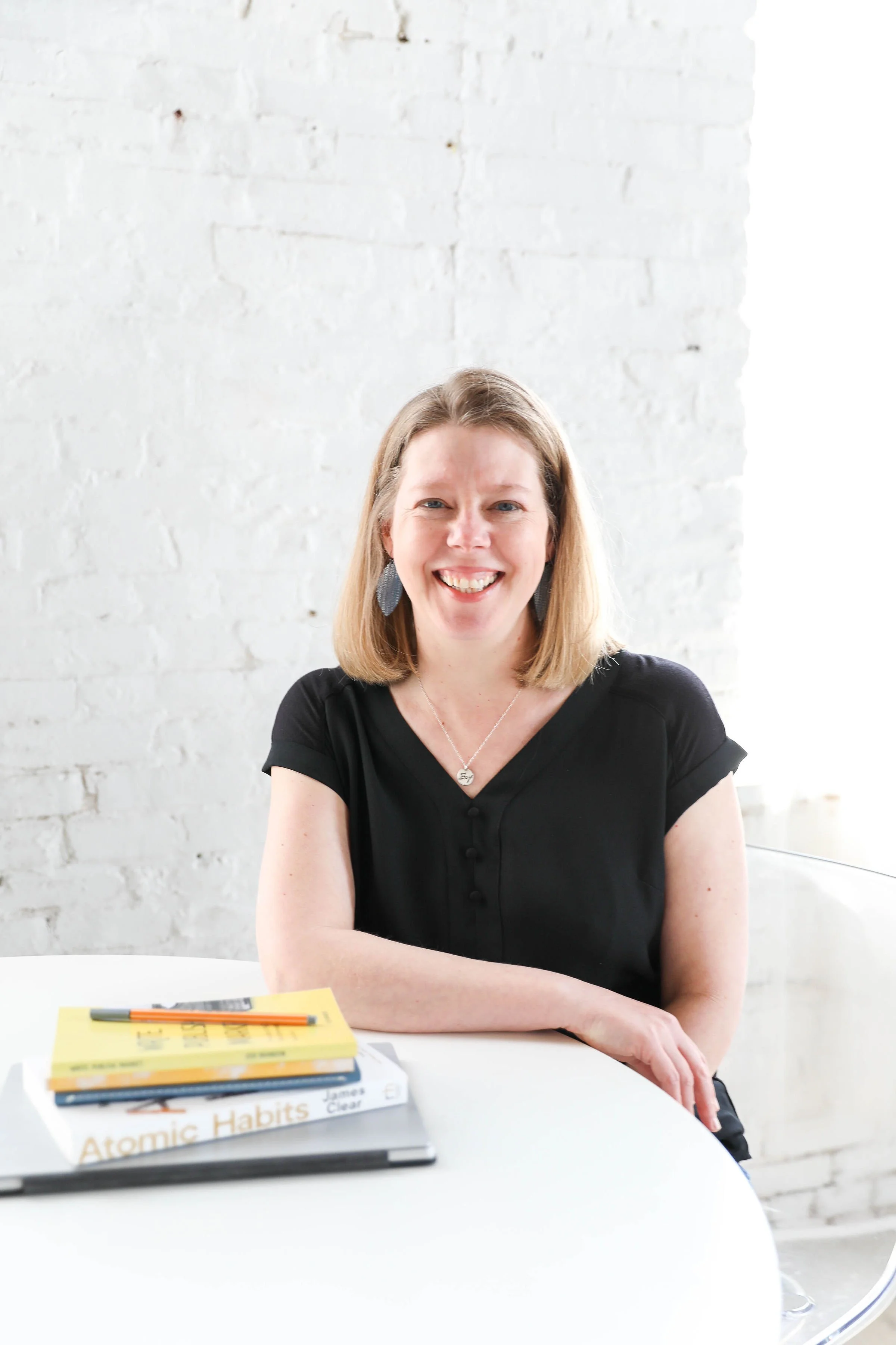 Jodi Brandon in a black short sleeve shirt sitting at a table with a stack of books and smiling