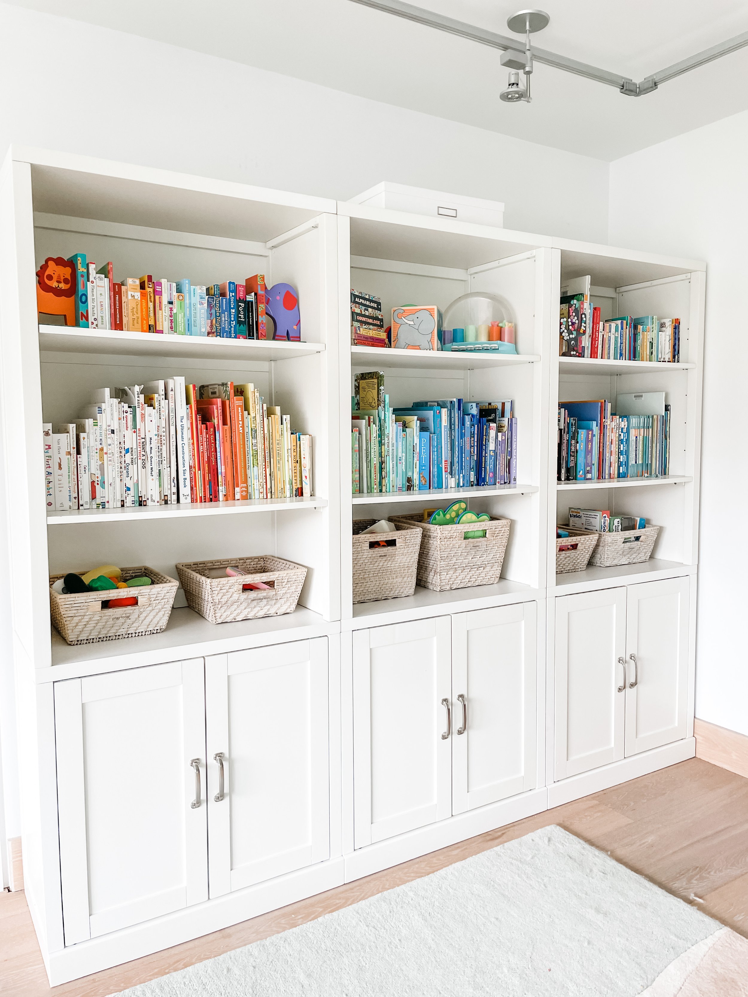 Built-in white cabinets and shelves with books arranged in a rainbow pattern