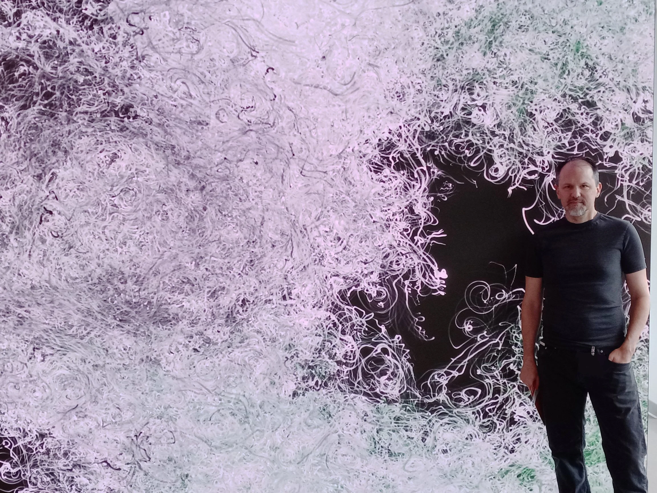 Artist Mark J Stock in front of his artwork on a high-resolution LED screen