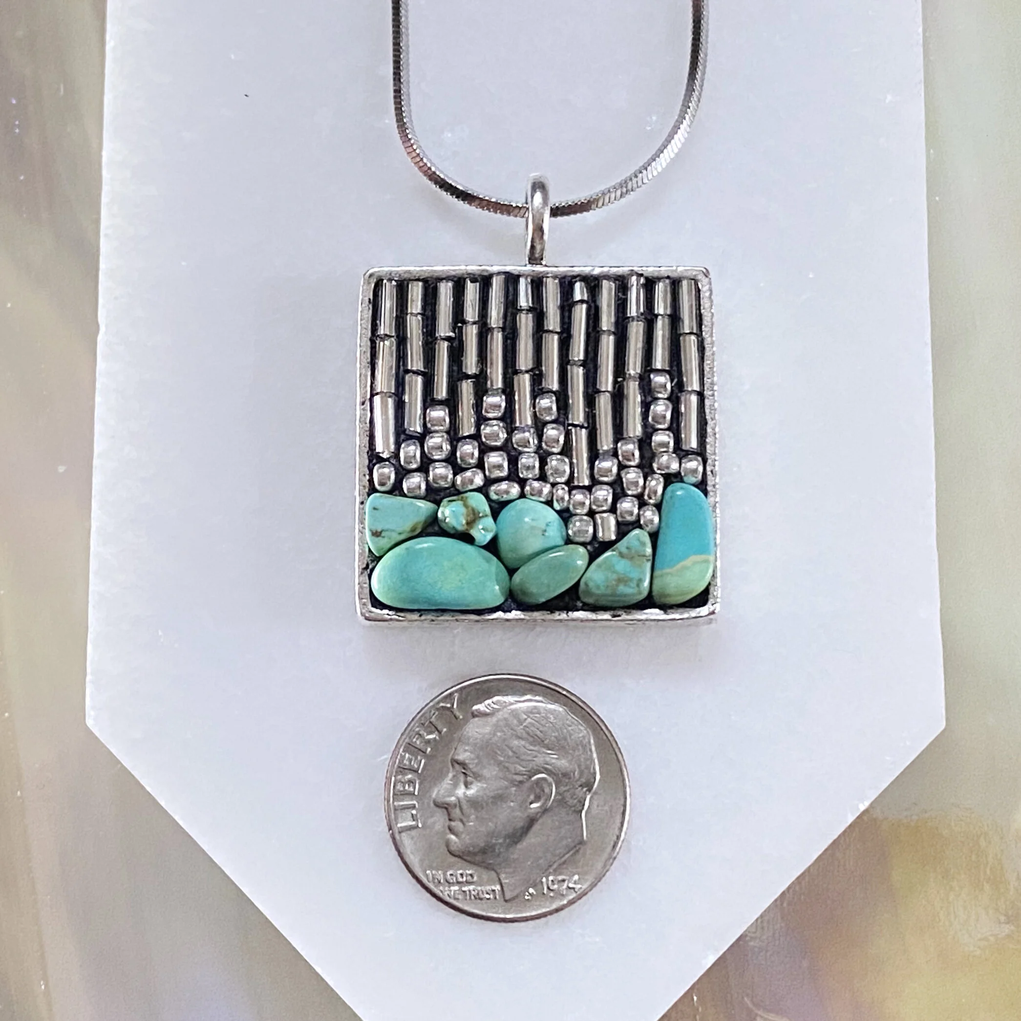 Square mosaic pendant by artist Dyanne Williams next to dime for size reference.