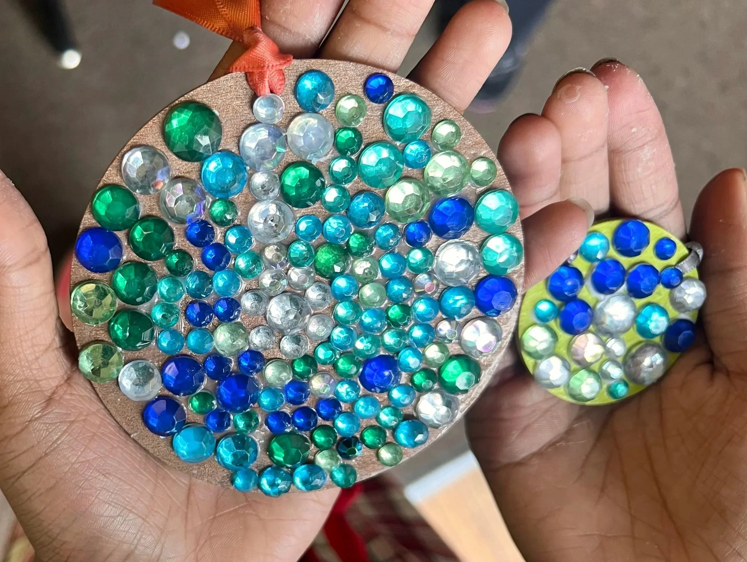 Child's hands holding two completed gem mosaic medallions made during the Cycles public art commission student participation project at Ida Nason Aronica Elementary School
