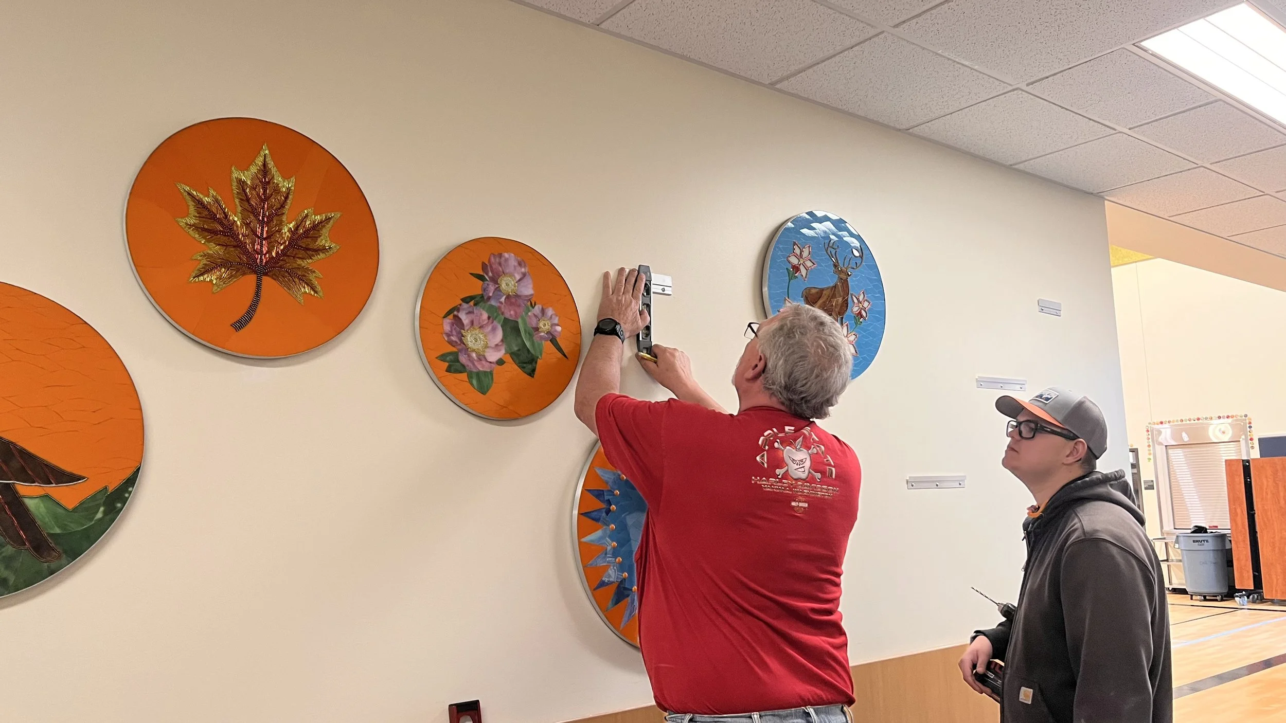 Head custodian using a level to accurately position French cleats for the Cycles public art mosaic installation at Ida Nason Aronica Elementary School in Ellensburg, Washington