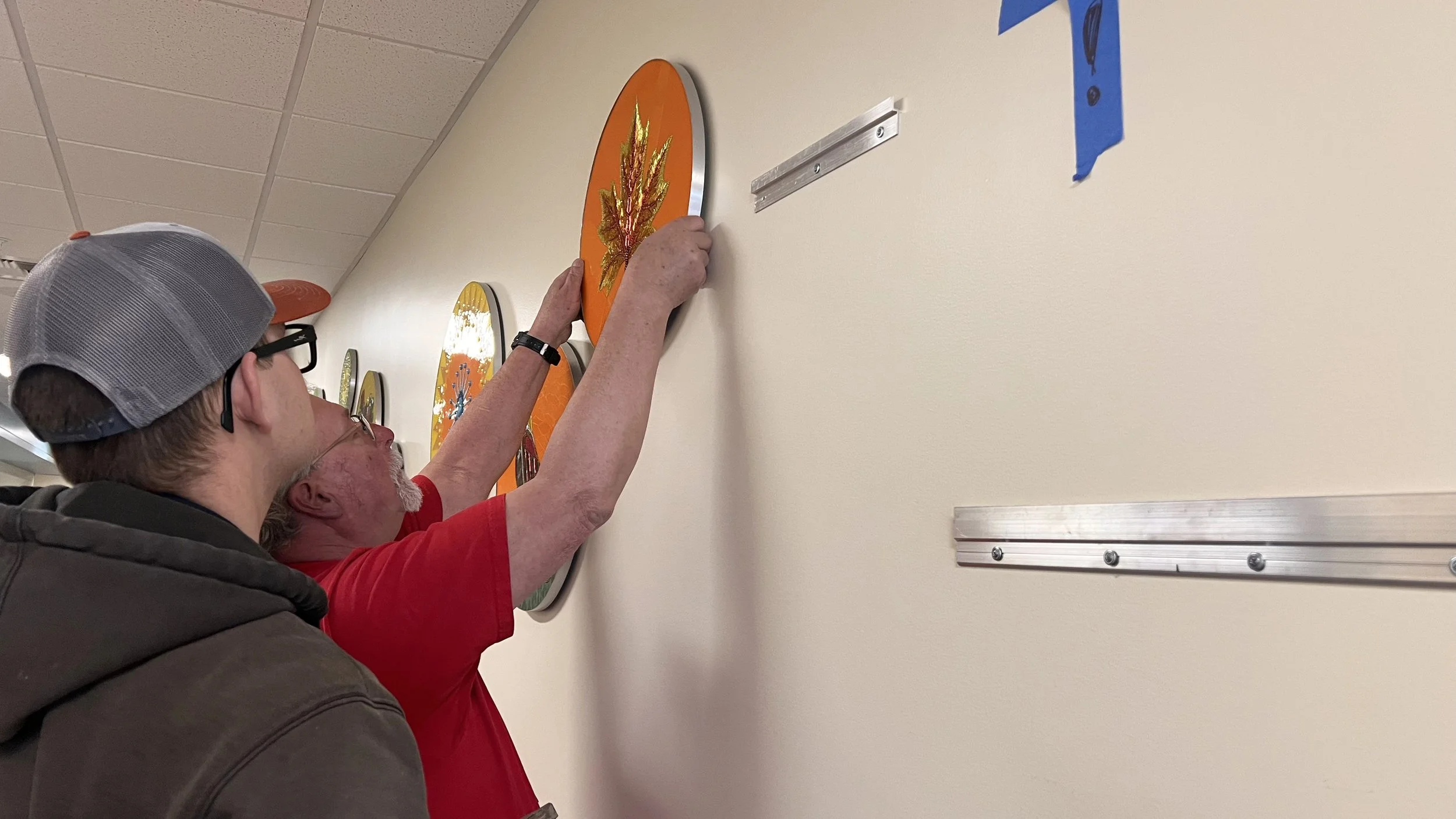 Head custodian hanging the fall leaf center panel of the Cycles public art mosaic at Ida Nason Aronica Elementary School in Ellensburg, Washington