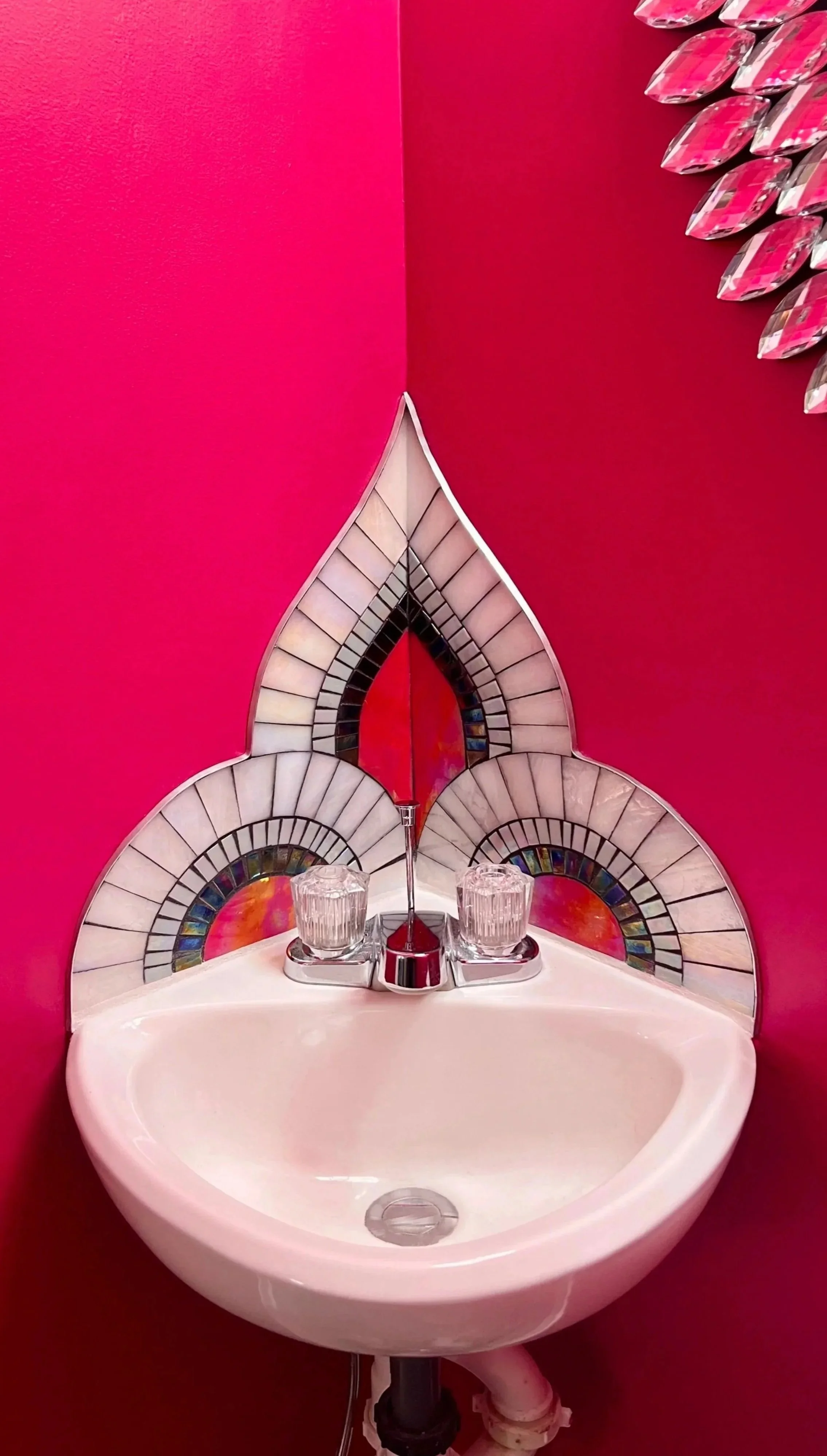 Art Deco mosaic backsplash above pedestal sink with centered peak motif in iridescent stained glass and metal edging