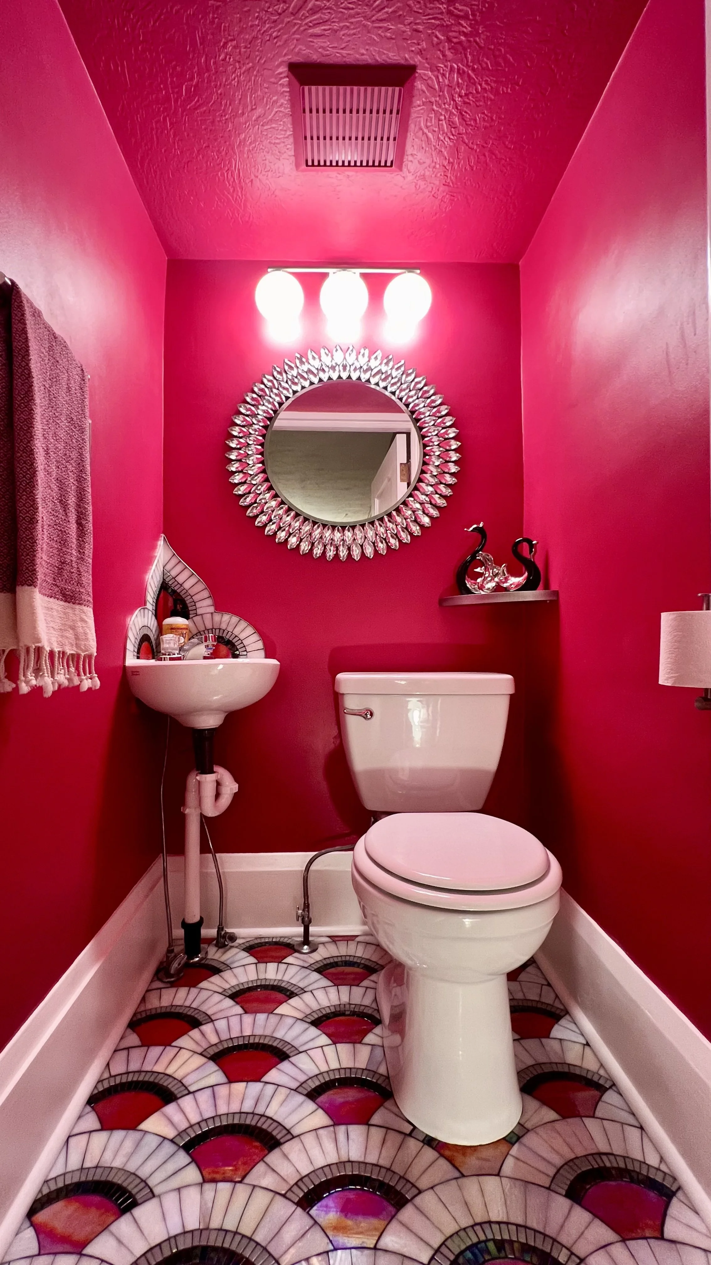 Art Deco mosaic powder room with magenta walls, iridescent stained glass scallop floor, crystal sunburst mirror, and black and silver swan sculptures, Canton Ohio