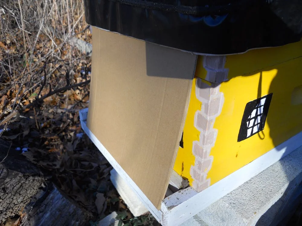 Here I am sneaking the cardboard up under the black wrap to keep it dry from snow and rain.