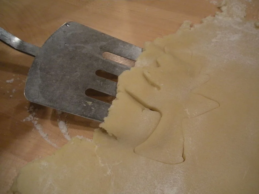 A regular spatula dusted in flour helps to remove the cookie once it is cut out of the dough.