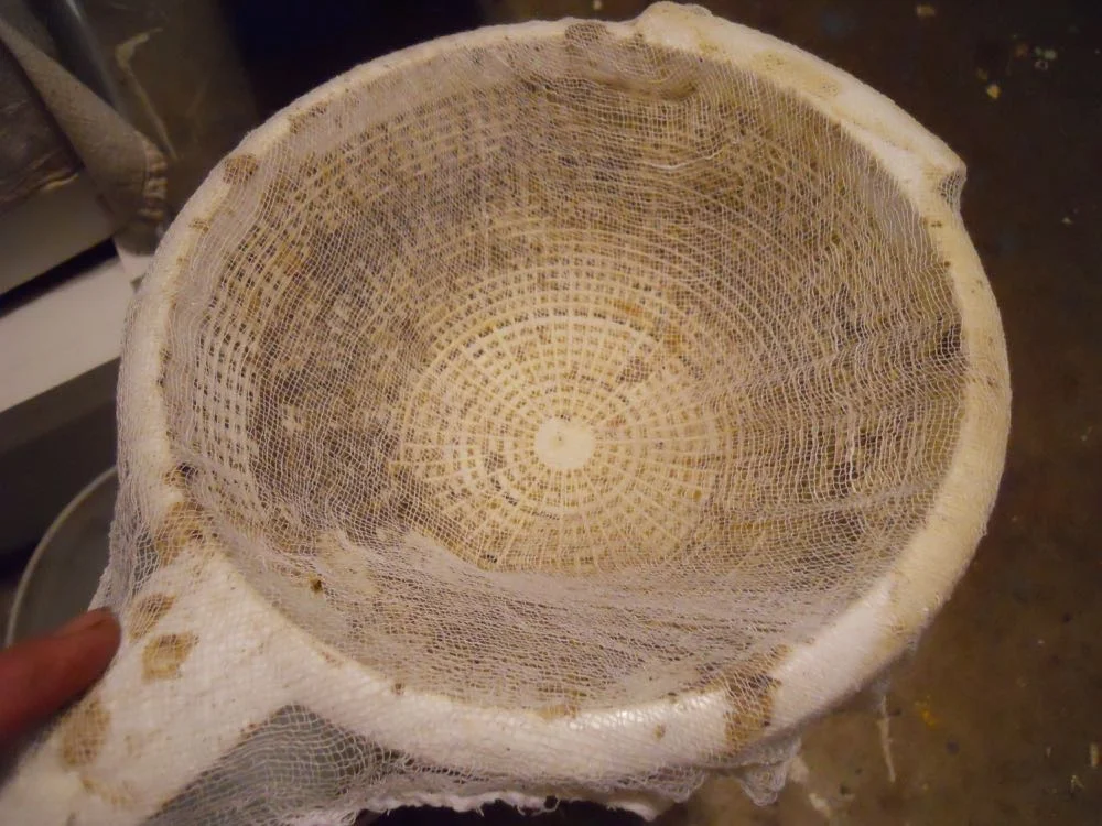 A piece of cheesecloth over an old colander helps catch debris as the wax soup pours through.