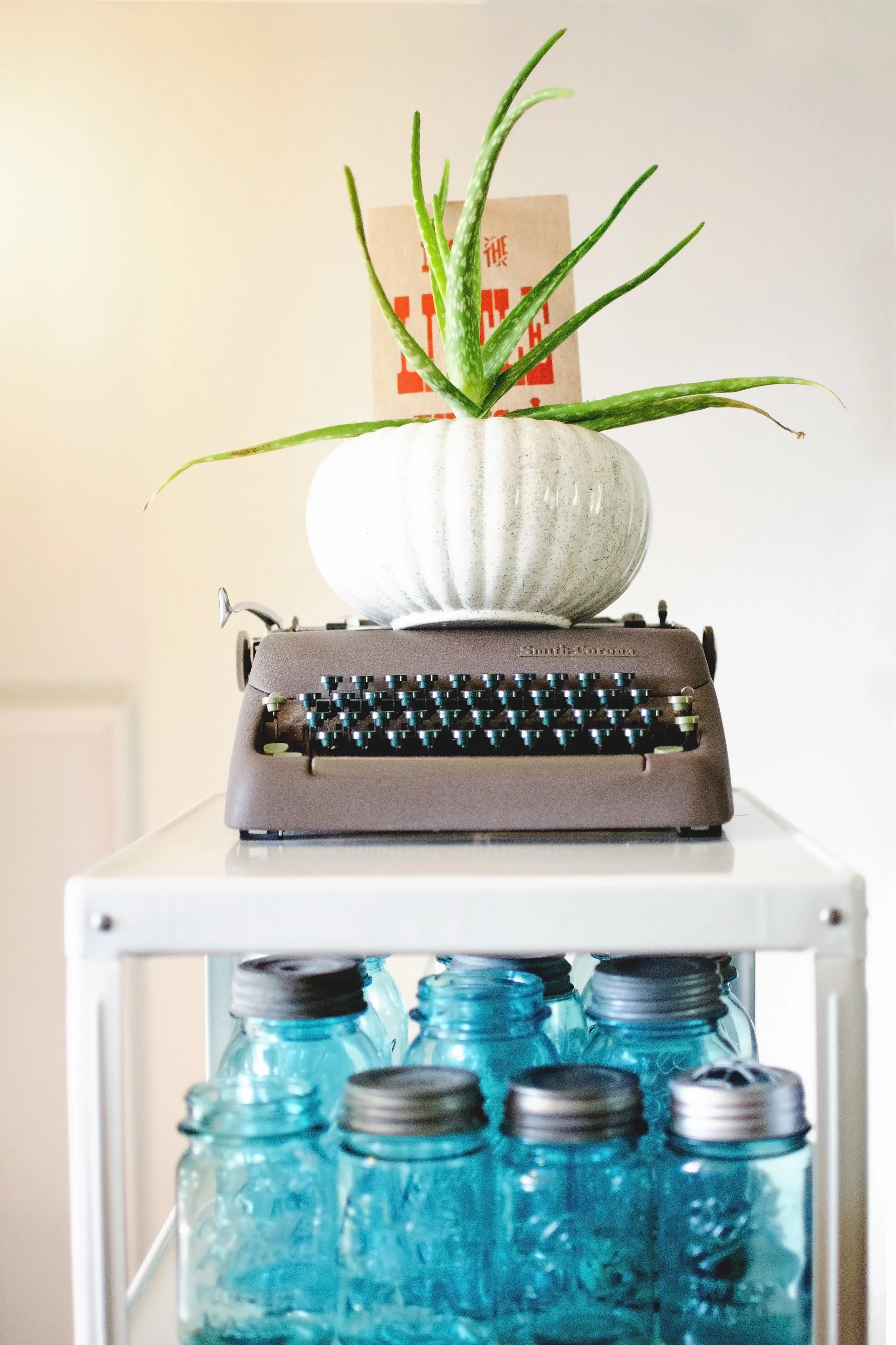 White metal shelving with blue ball jars, a vintage typewriter, and potted plant. H.Prall & Co. | hprallandco.com