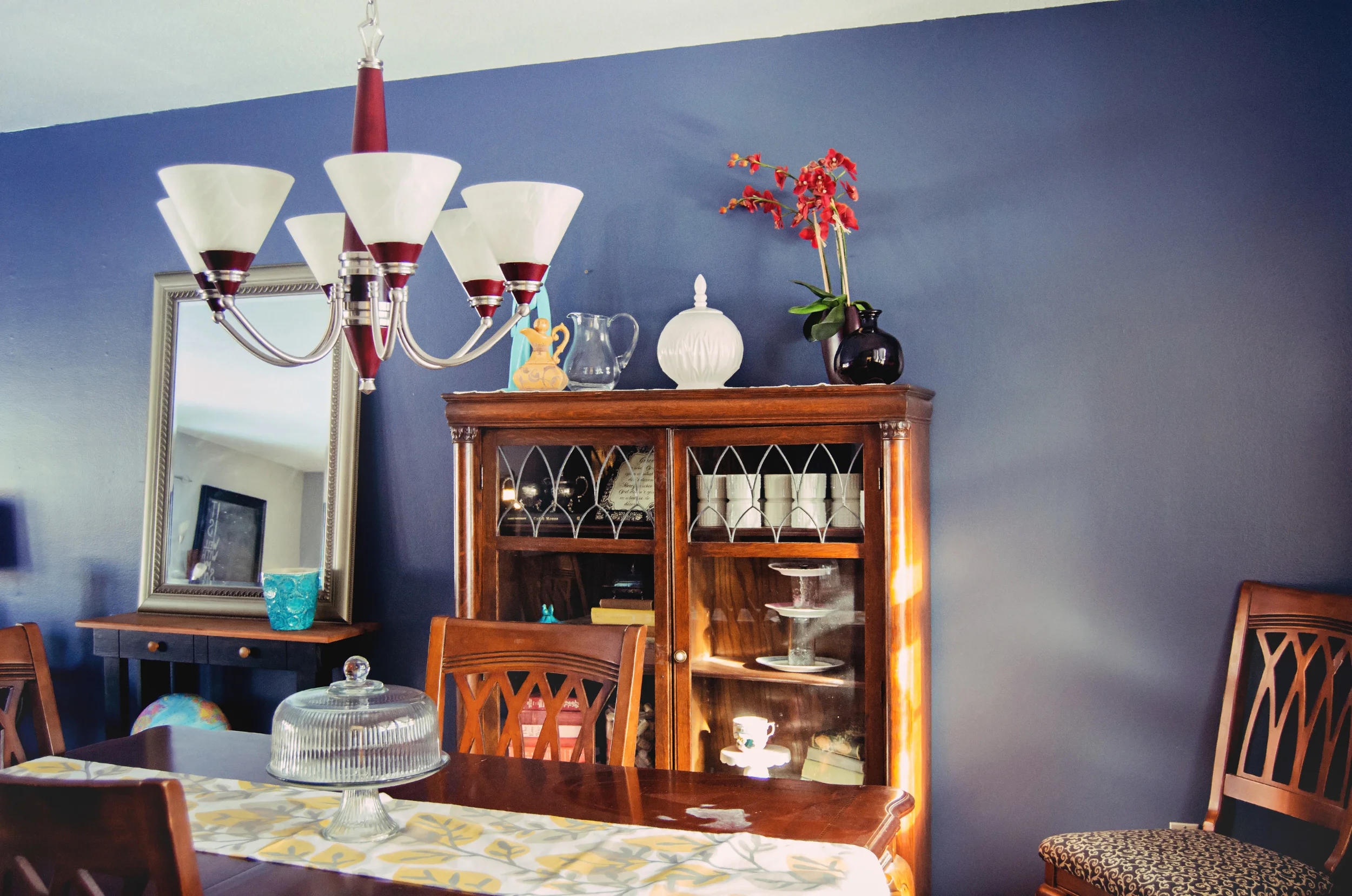 Blue dining room wall with pops of red in the light fixture and accessories. | hprallandco.com