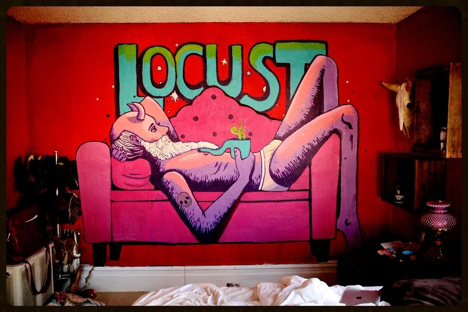 A vibrant mural of a pink deviant, with a beard and elongated limbs, lying on a pink sofa. The background features the word 'LOCUST' in large colorful letters on a red wall.