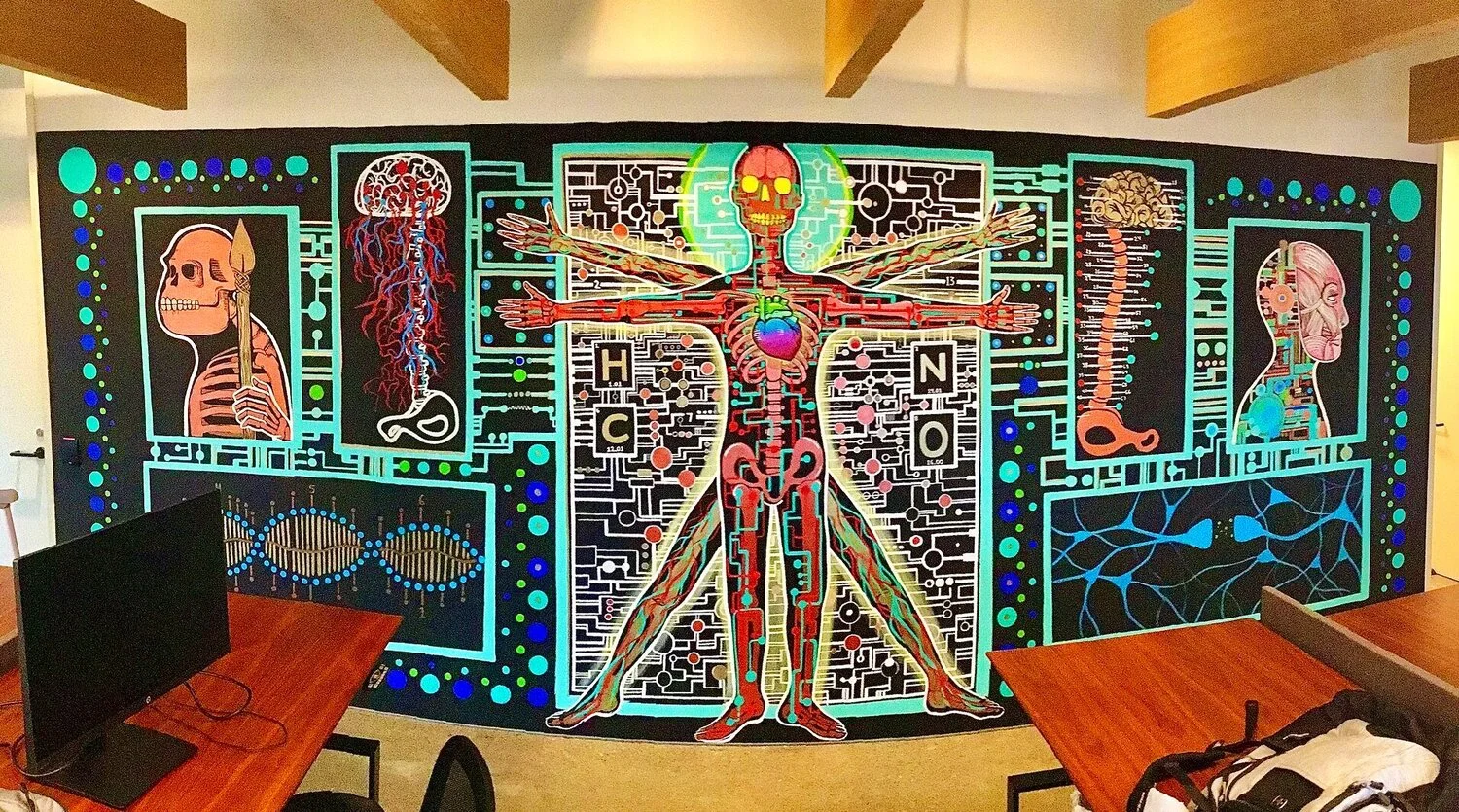Colorful mural depicting a human anatomy with labeled brain, heart, lungs, and other organs, surrounded by circuitry patterns and scientific symbols.