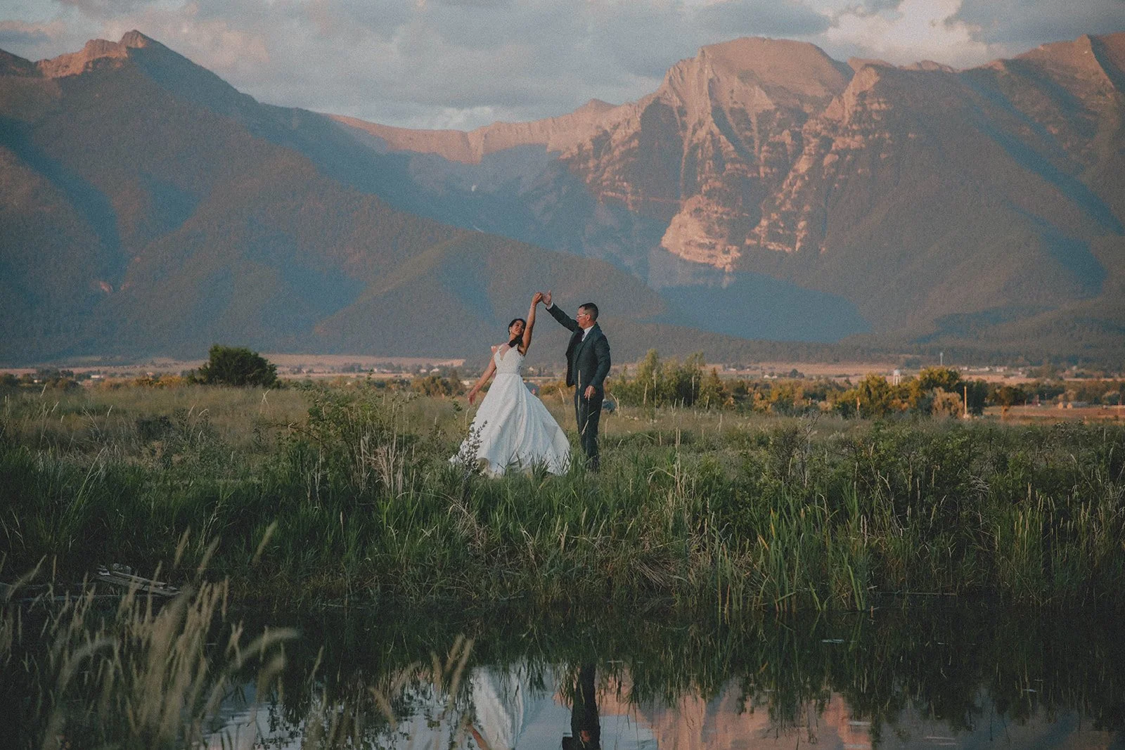 Bride and groom dance next to the seasonal pond at the Rugged Horizon wedding venue in St. Ignatius, Montana, as the sun sets on the Mission Mountains in the background. Photo by SJ Harris Photography.
